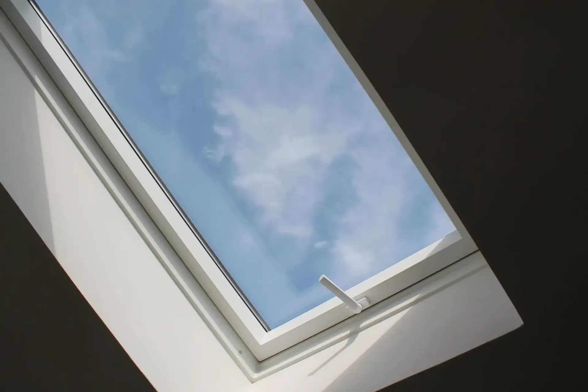 Skylight in a white frame, angled view of a blue sky with clouds.