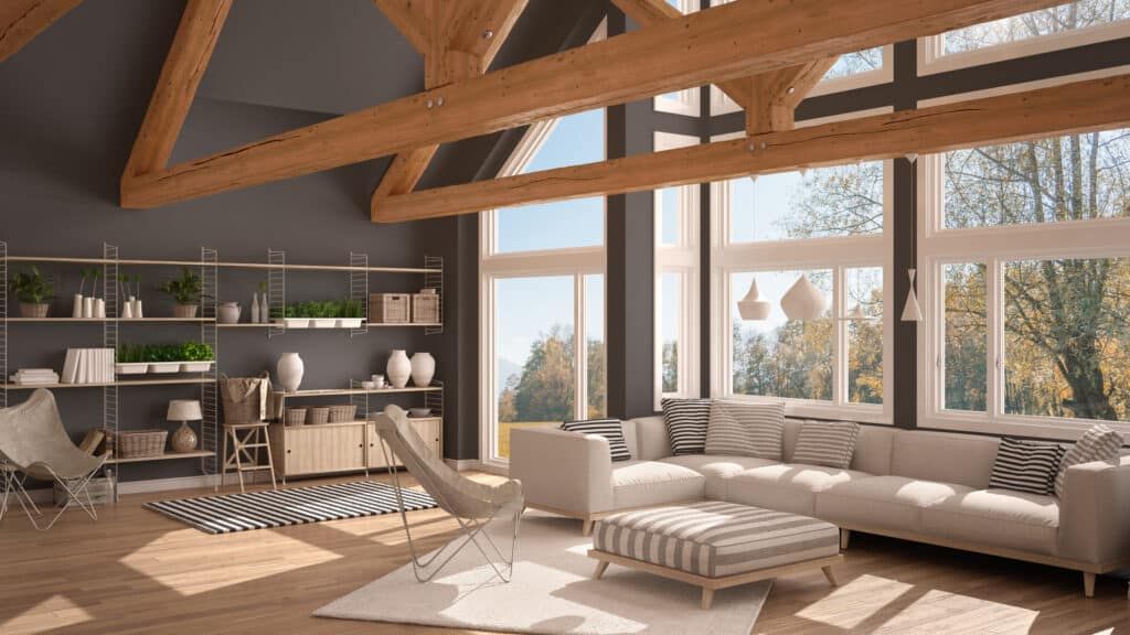 Living room with large windows, wood beams, gray walls, and light-colored furniture, overlooking a natural landscape.