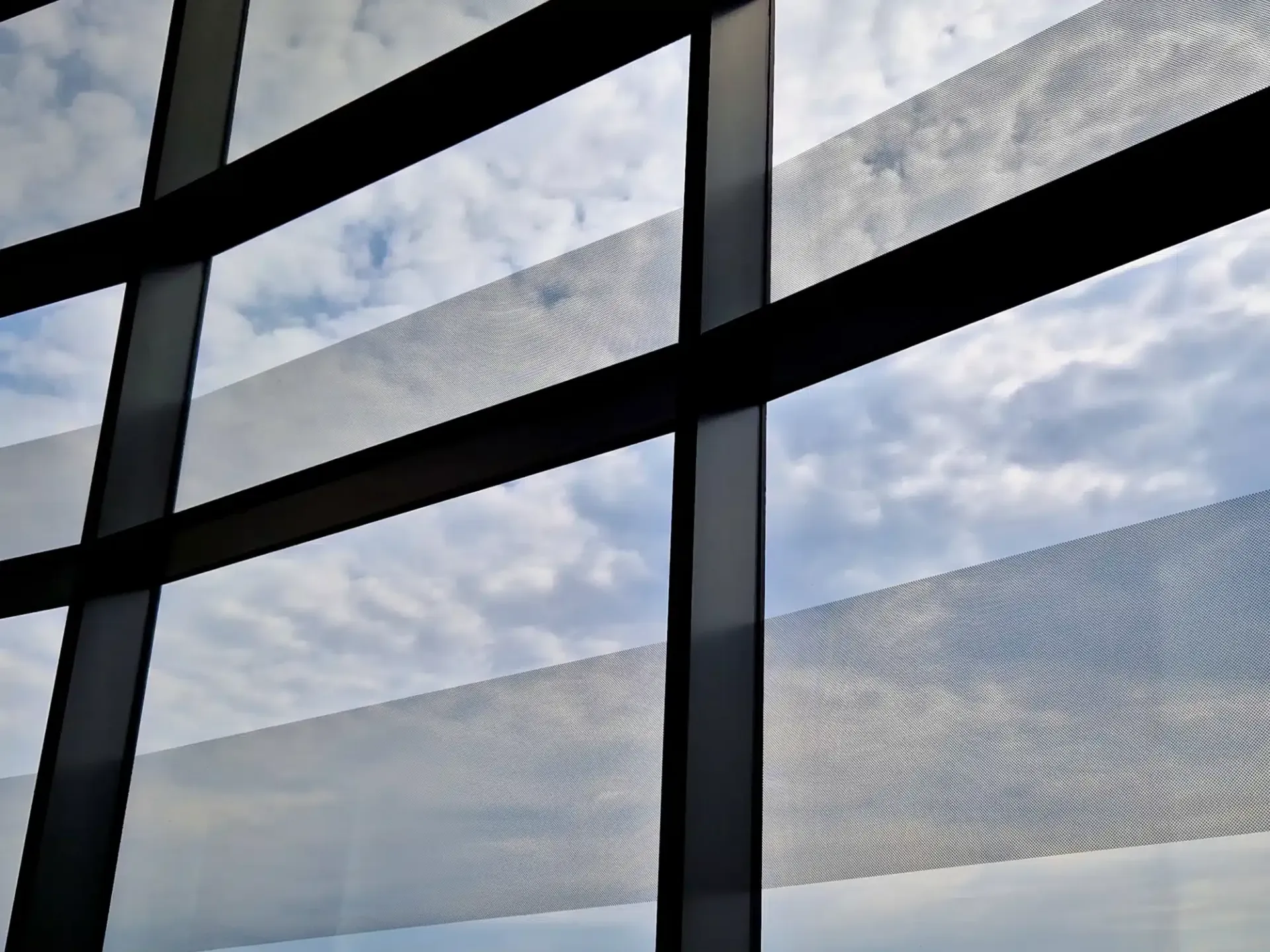 View through a window with horizontal bands of mesh, against a cloudy sky. Black frames.