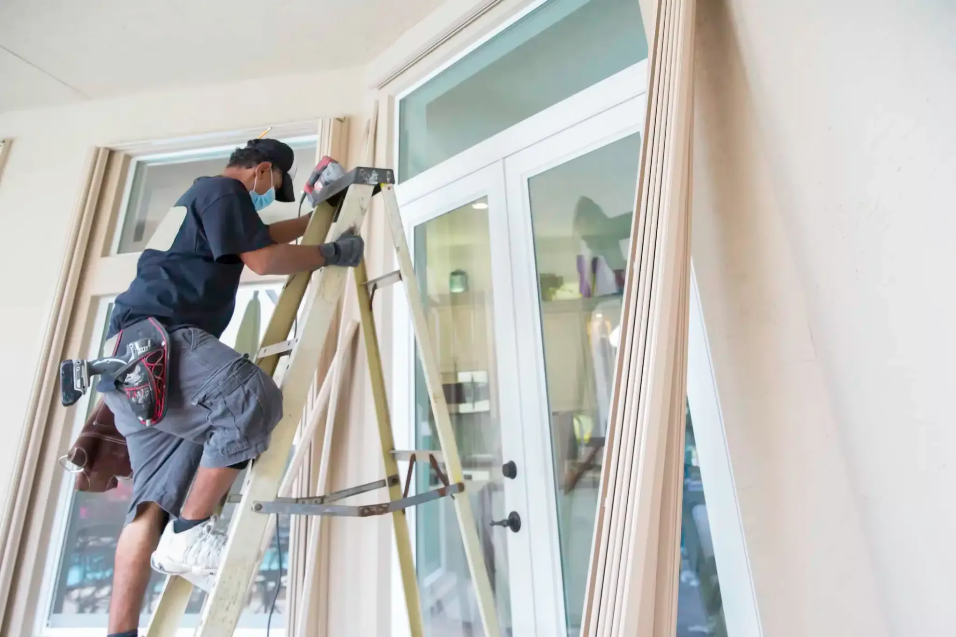 Window cleaner on ladder washing glass door inside a building.