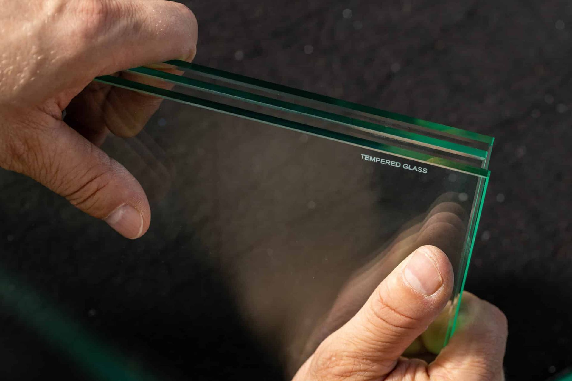 Hands holding a stack of clear glass sheets, showing edges and a logo.