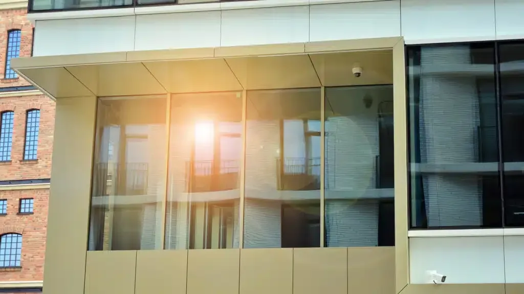 Modern building with large windows reflecting sunlight and another building.