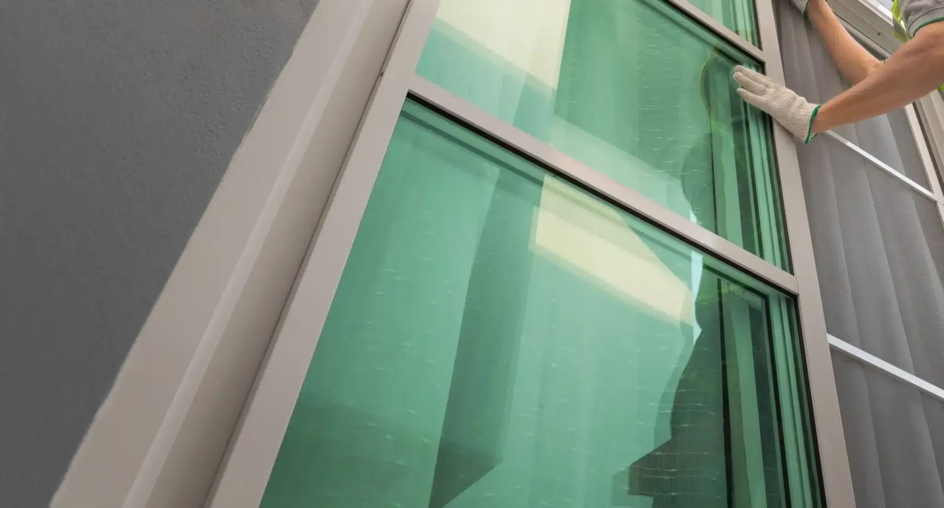 Person wearing gloves cleaning a green-tinted window from the outside.