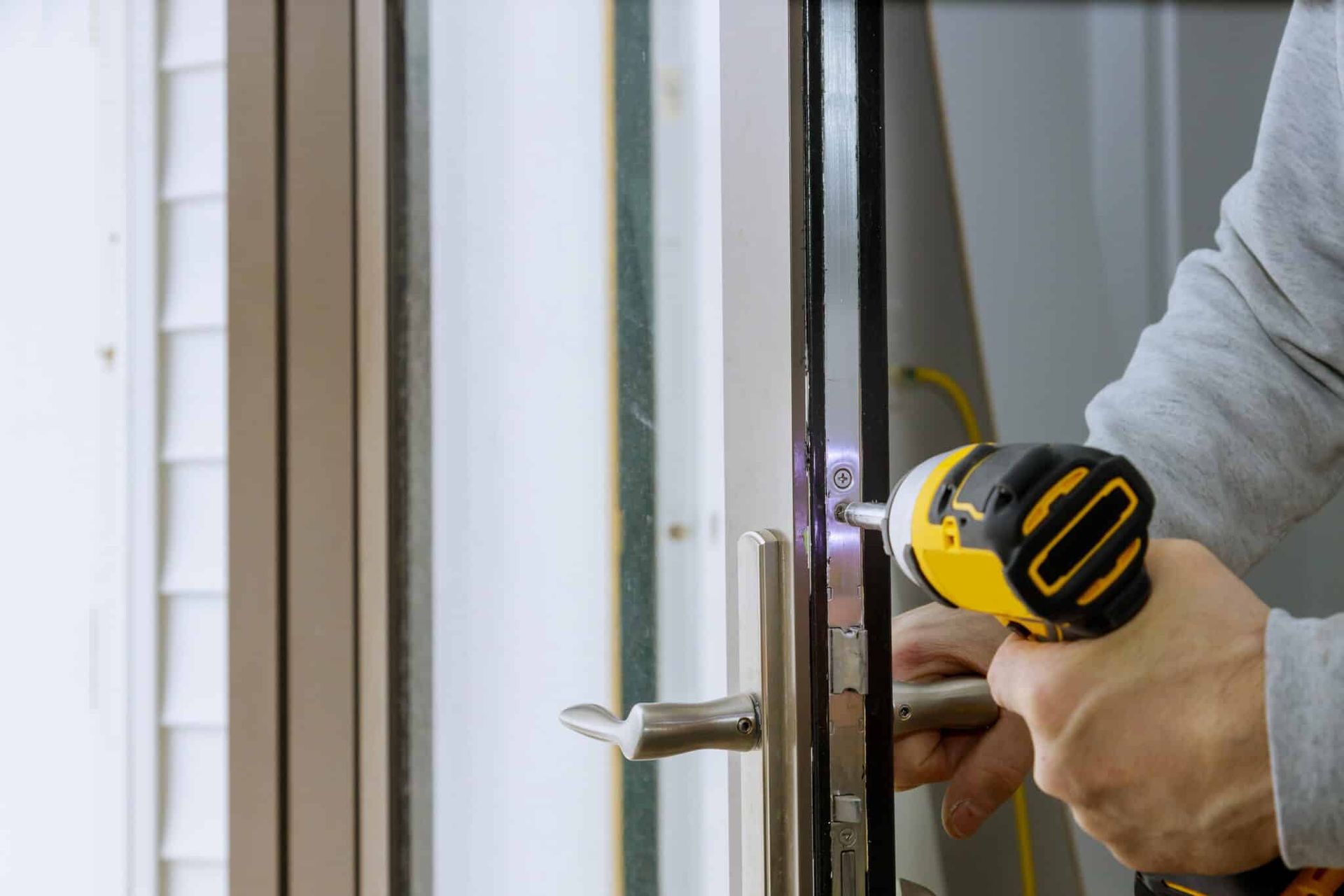 Person using a yellow drill to install a door handle on a glass door.