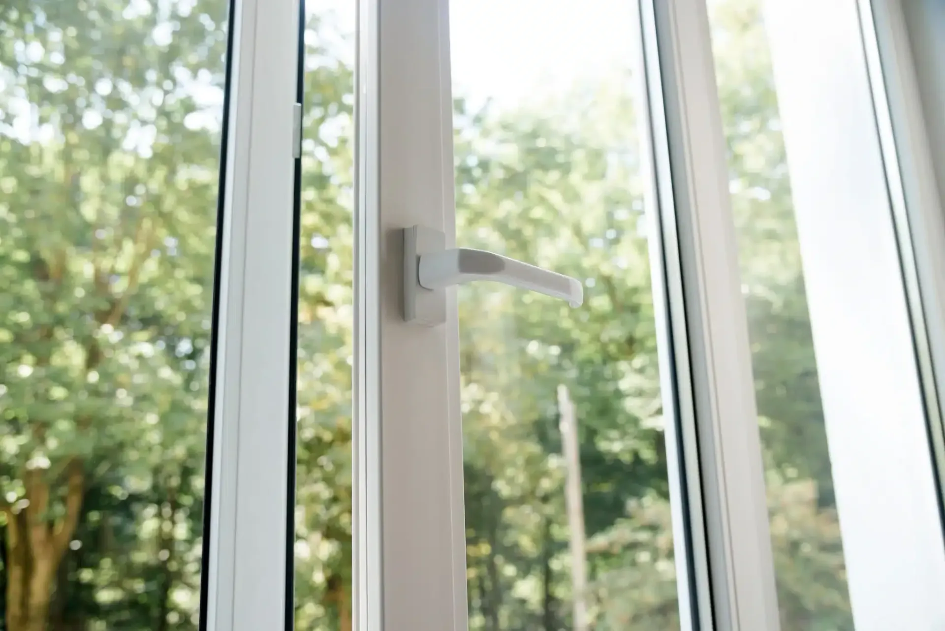 White window with a partially open handle, view of green trees outside.