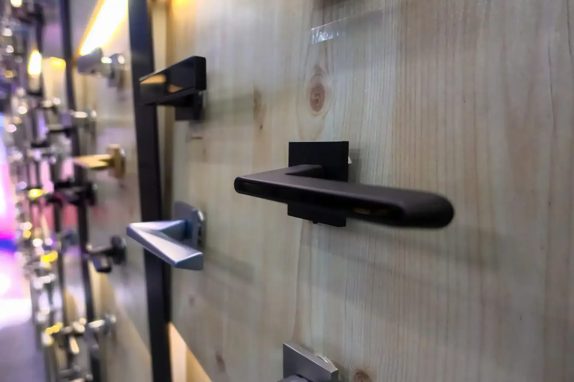 Door handles on display, mounted on a light-colored wooden panel, with various shapes and colors.
