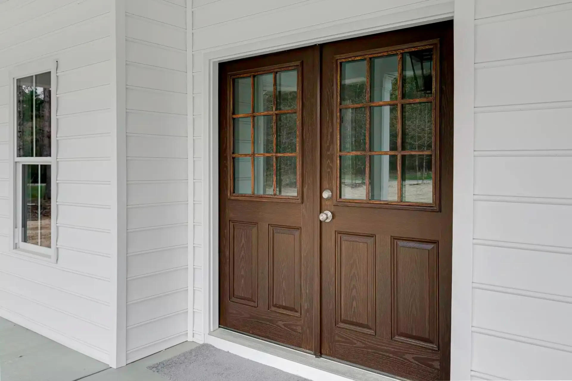 White building with brown double doors, glass pane windows, and a small side window.