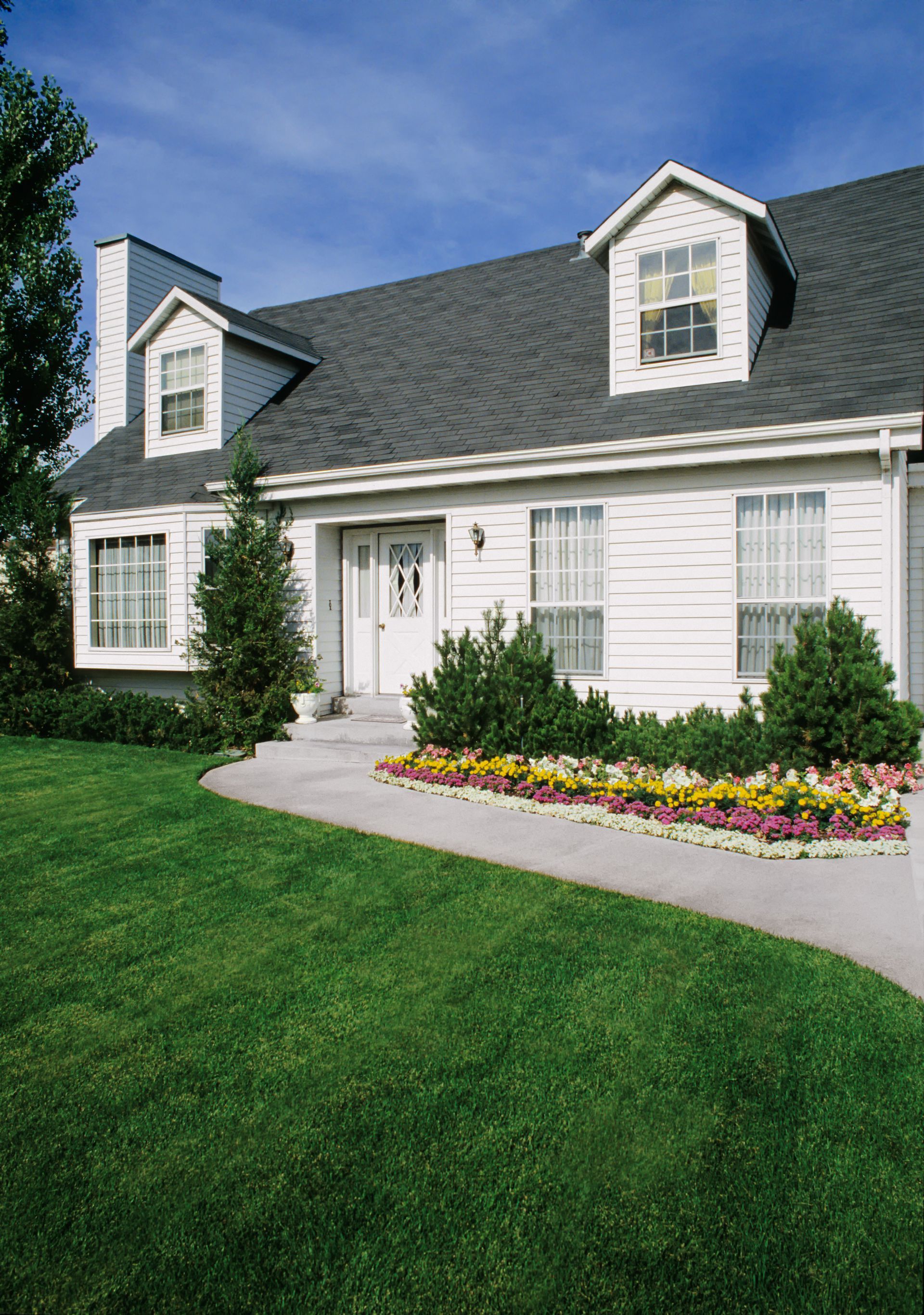 White house with dark roof, dormers, and a well-manicured lawn and garden pathway.