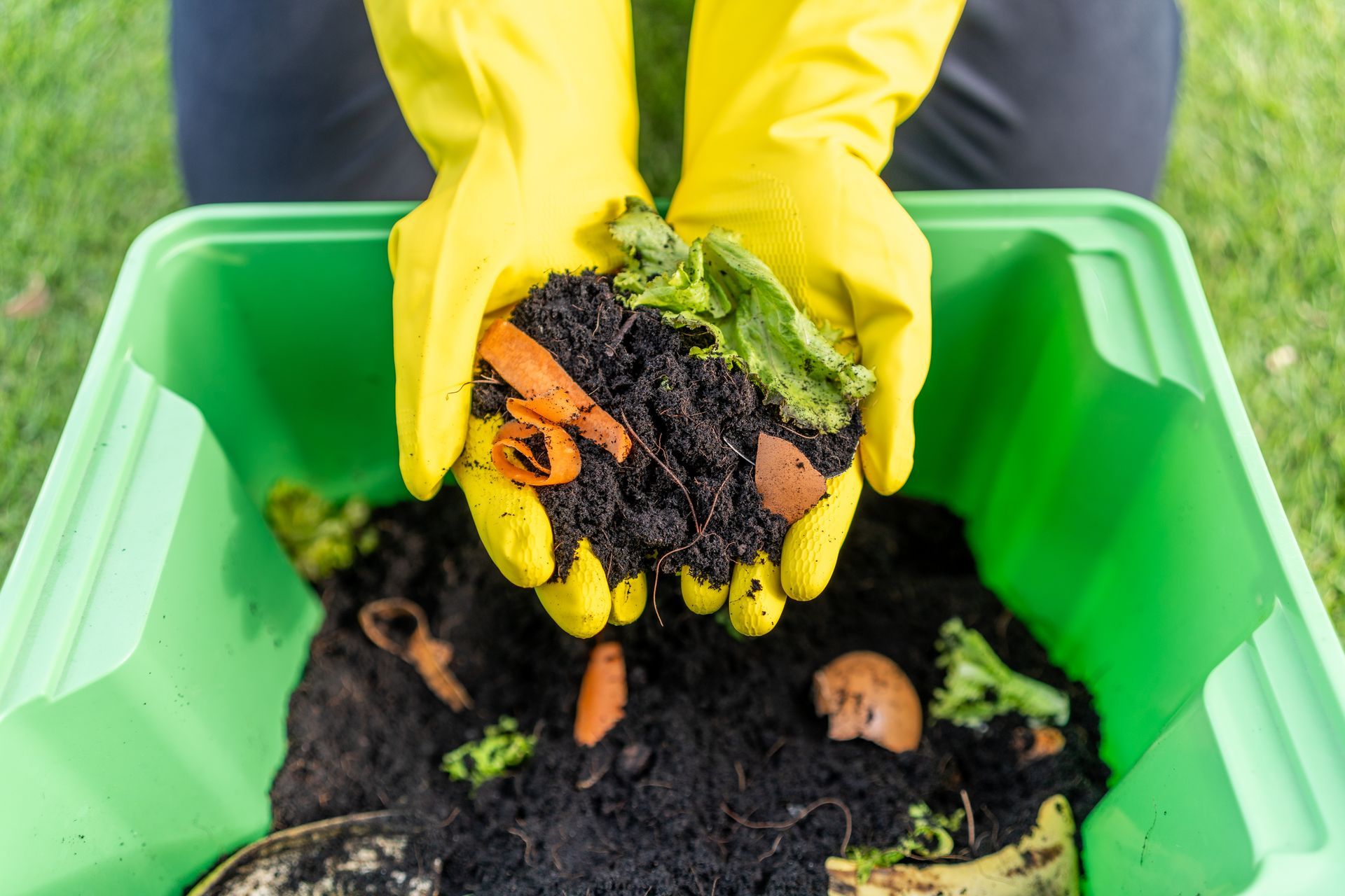 Person in yellow gloves holding compost from a green bin, showcasing vegetable scraps.