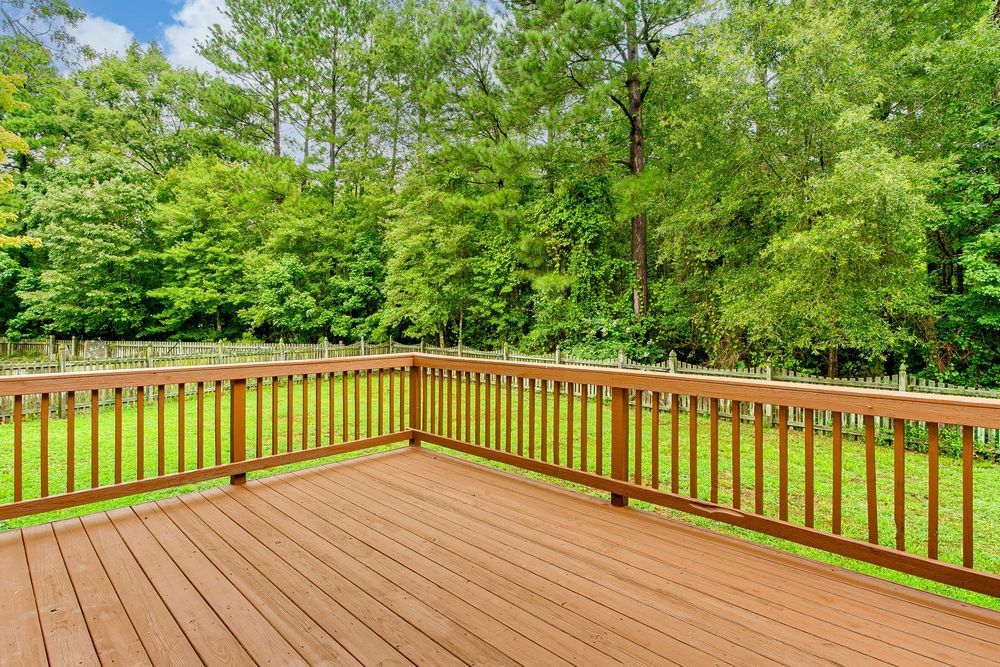 An empty wooden deck with a wooden railing overlooking a lush green field.
