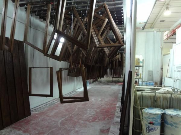 Cornici di legno appese in una cabina di verniciatura industriale, probabilmente per la finitura o la colorazione.