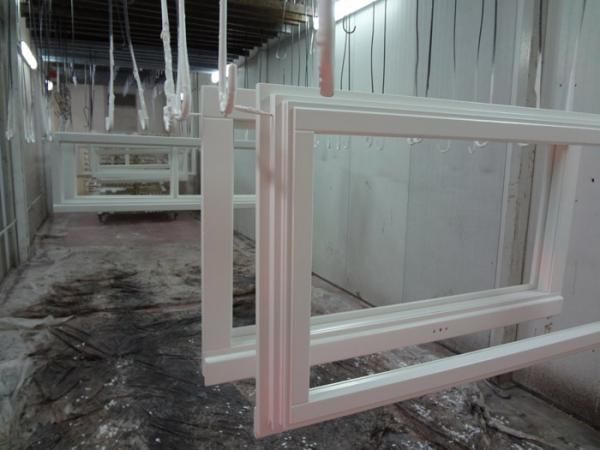 Cornici bianche di finestre appese all'interno di una cabina di verniciatura.