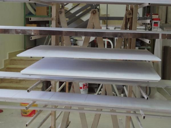 Pannelli dipinti di bianco ad asciugare su rastrelliere in un laboratorio.