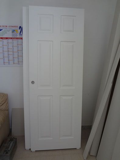 Porta interna bianca a sei pannelli appoggiata a una parete, in una stanza con calendario e modanature.