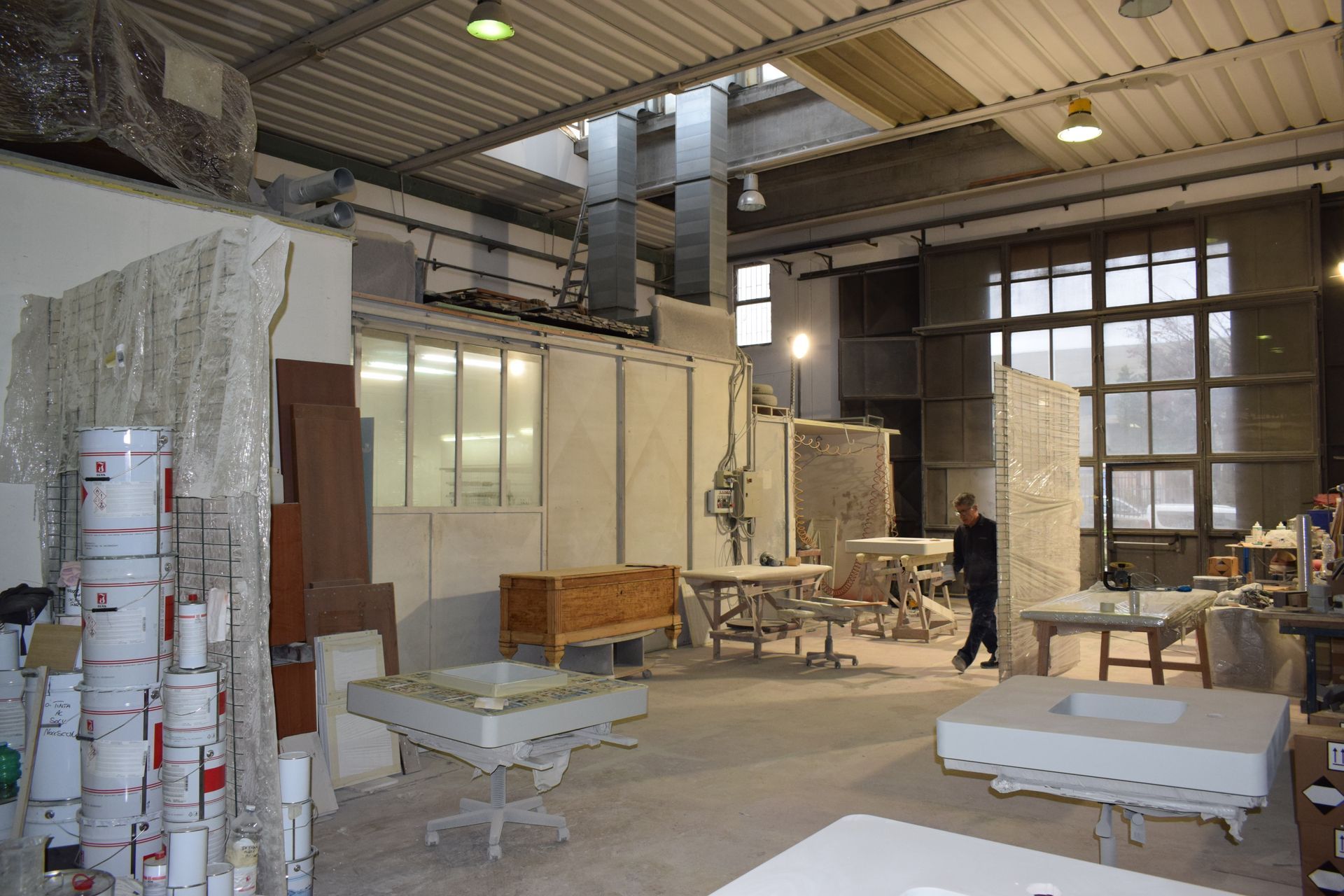 Interno del laboratorio con tavoli e attrezzature. Una persona cammina attraverso lo spazio. Luce naturale e intensa.