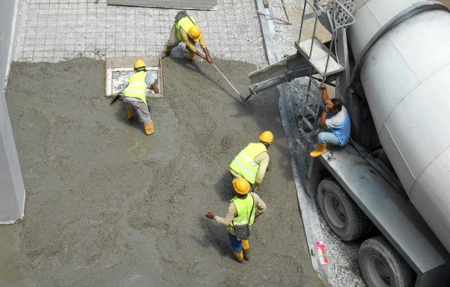 Construction workers in high-visibility vests spread wet concrete from a mixer truck on a building site.