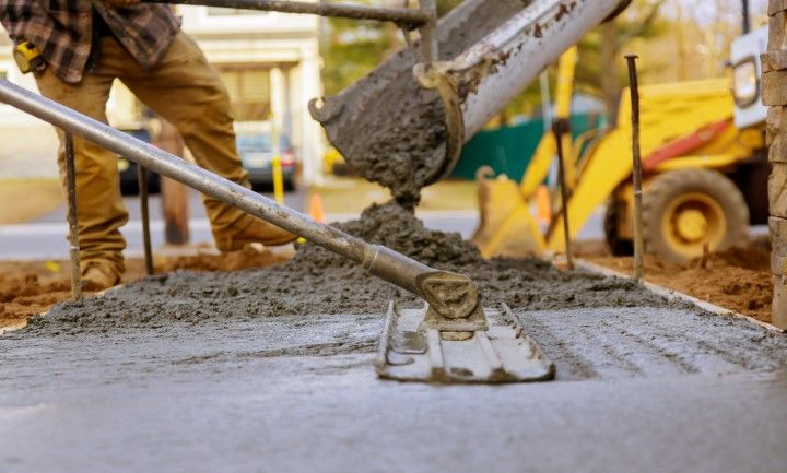 A construction worker uses a long-handled concrete float to smooth freshly poured concrete from a truck chute.
