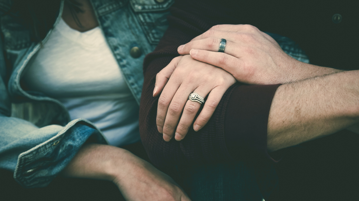 A man and a woman are holding hands with rings on their fingers.