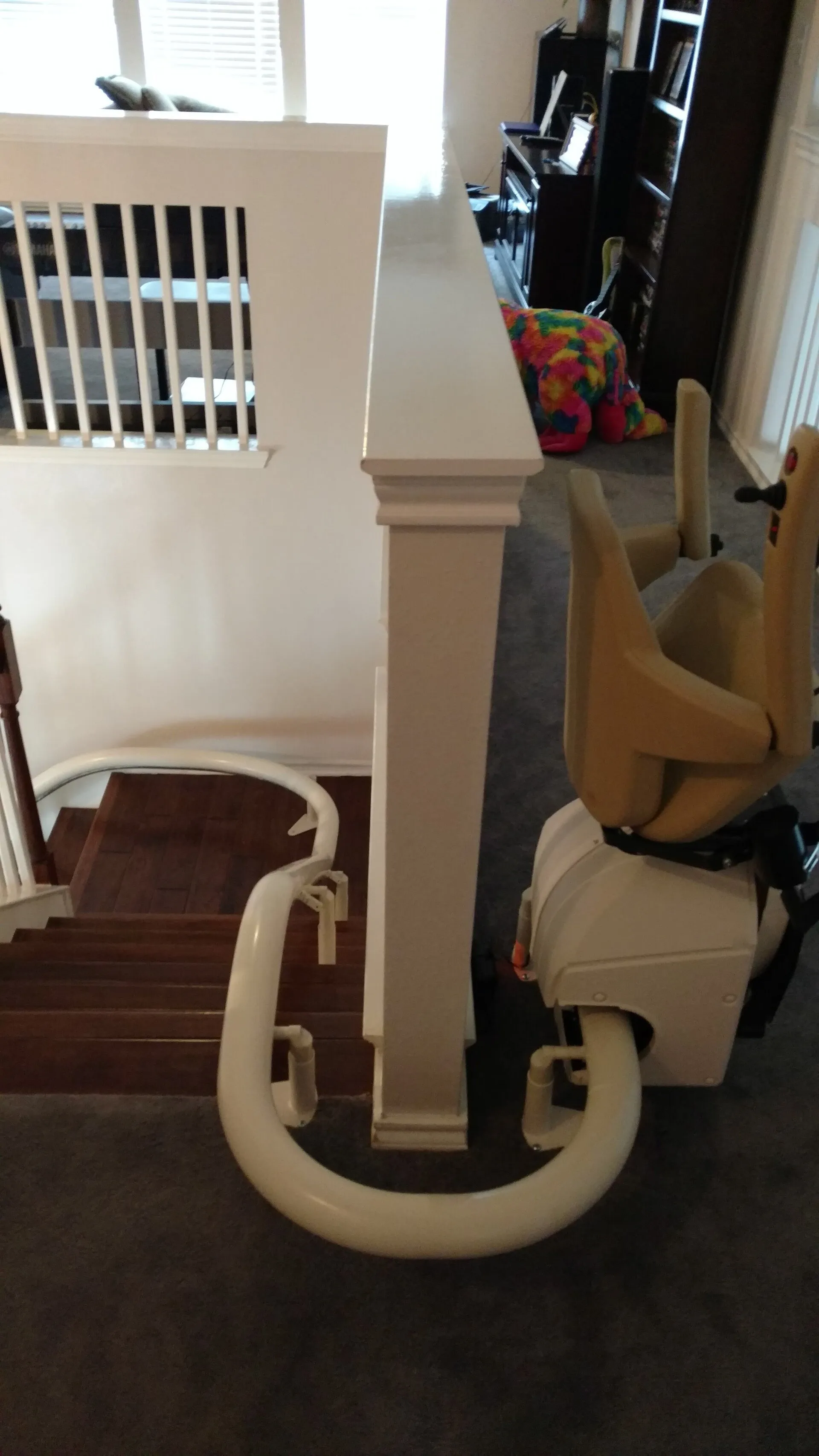 Staircase with a stairlift; view from above. White rails and a beige chair.