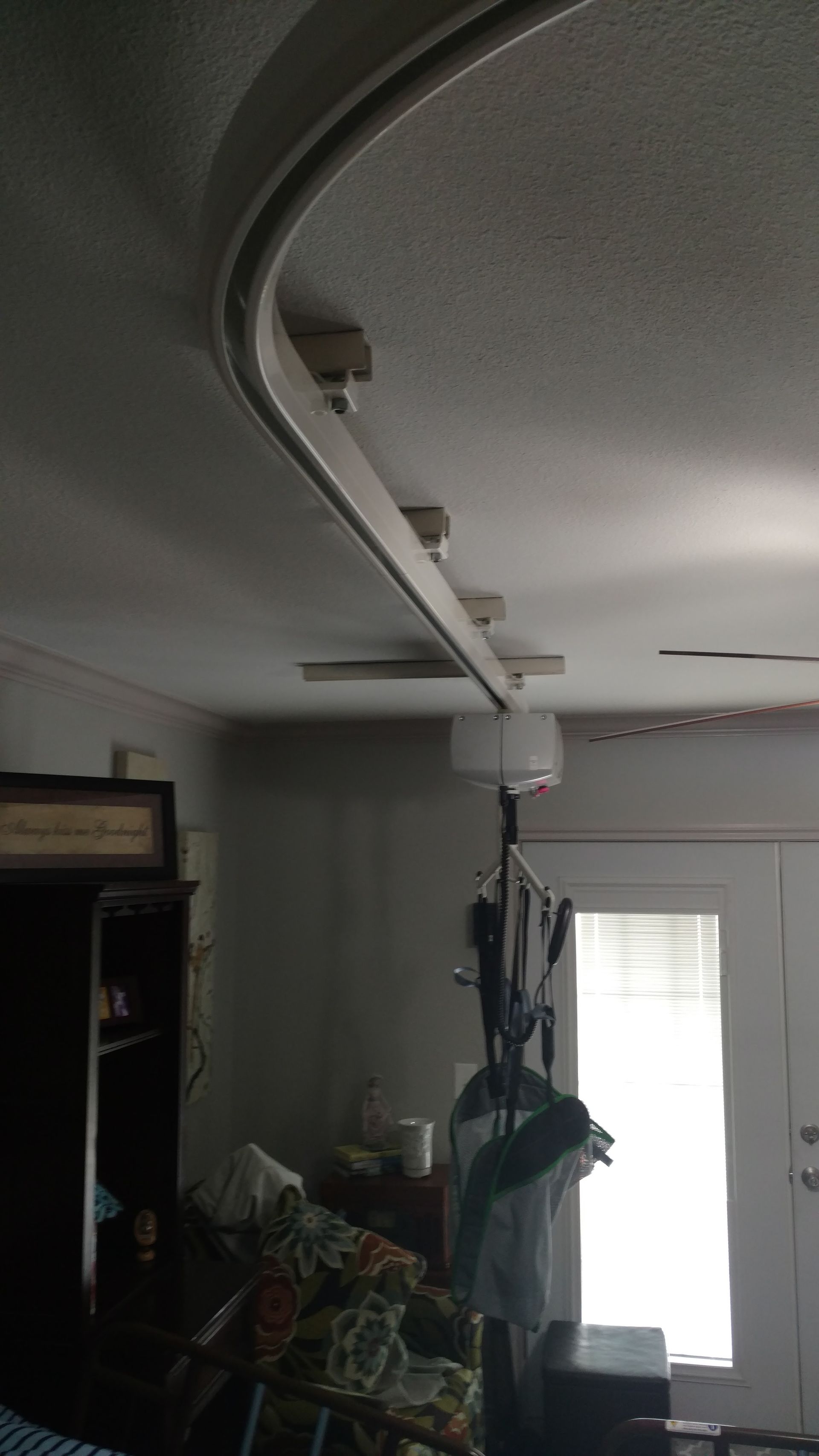 Curved ceiling track, possibly for a lift, in a room with a lamp and doorway.