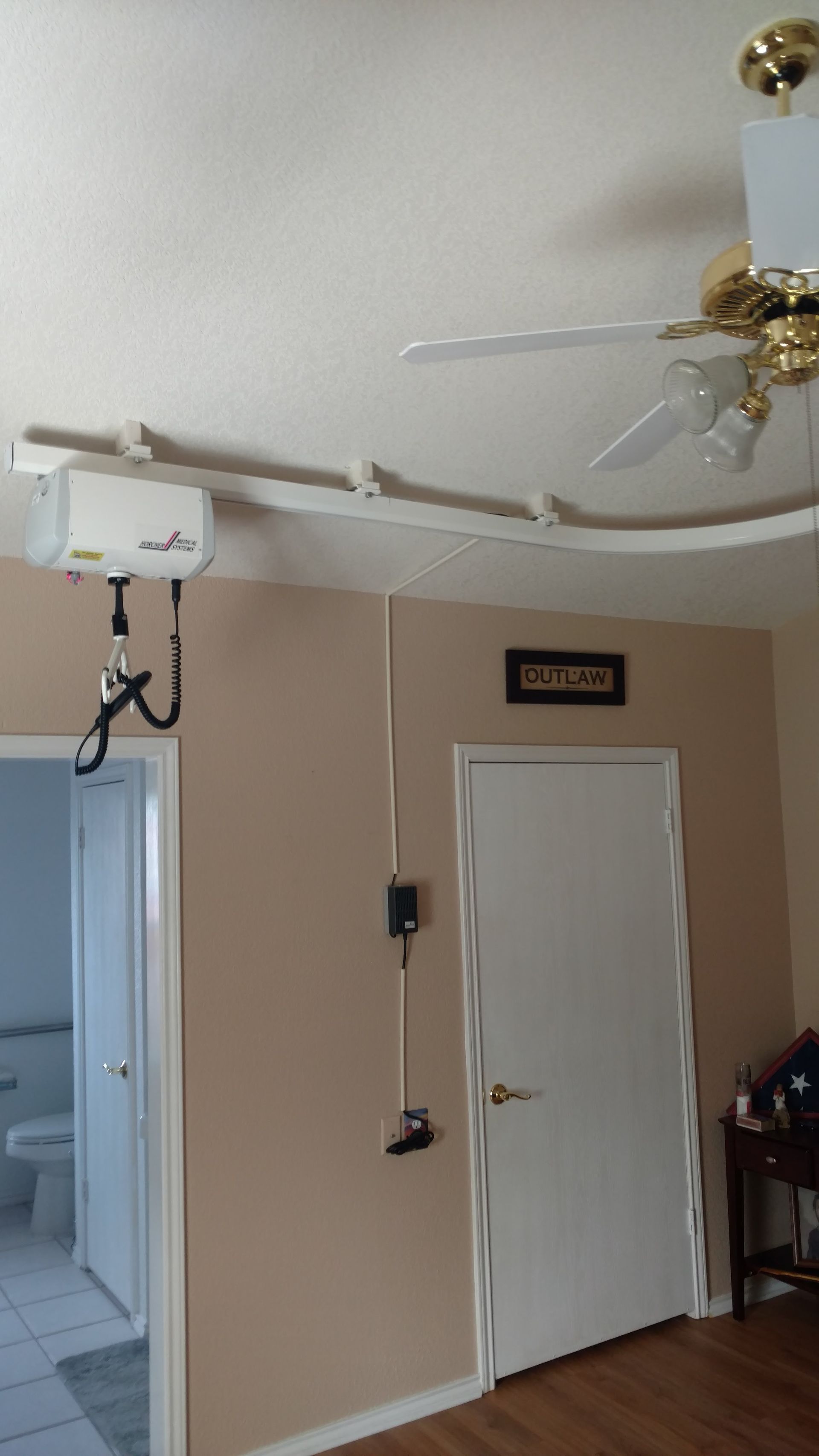 Ceiling-mounted patient lift system in a home, over doorway and near a closed white door.