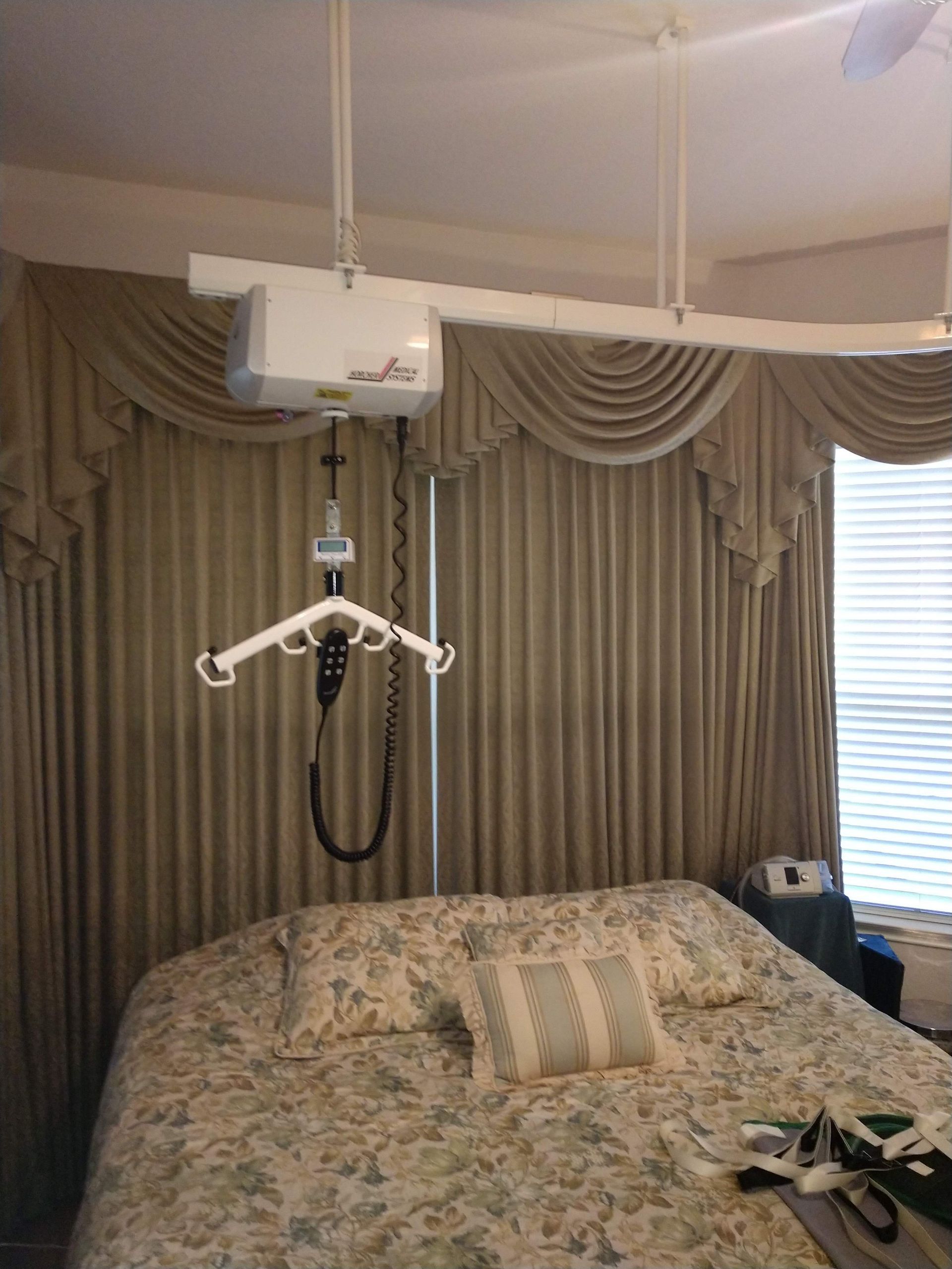 Ceiling-mounted patient lift over a bed in a bedroom with curtains.