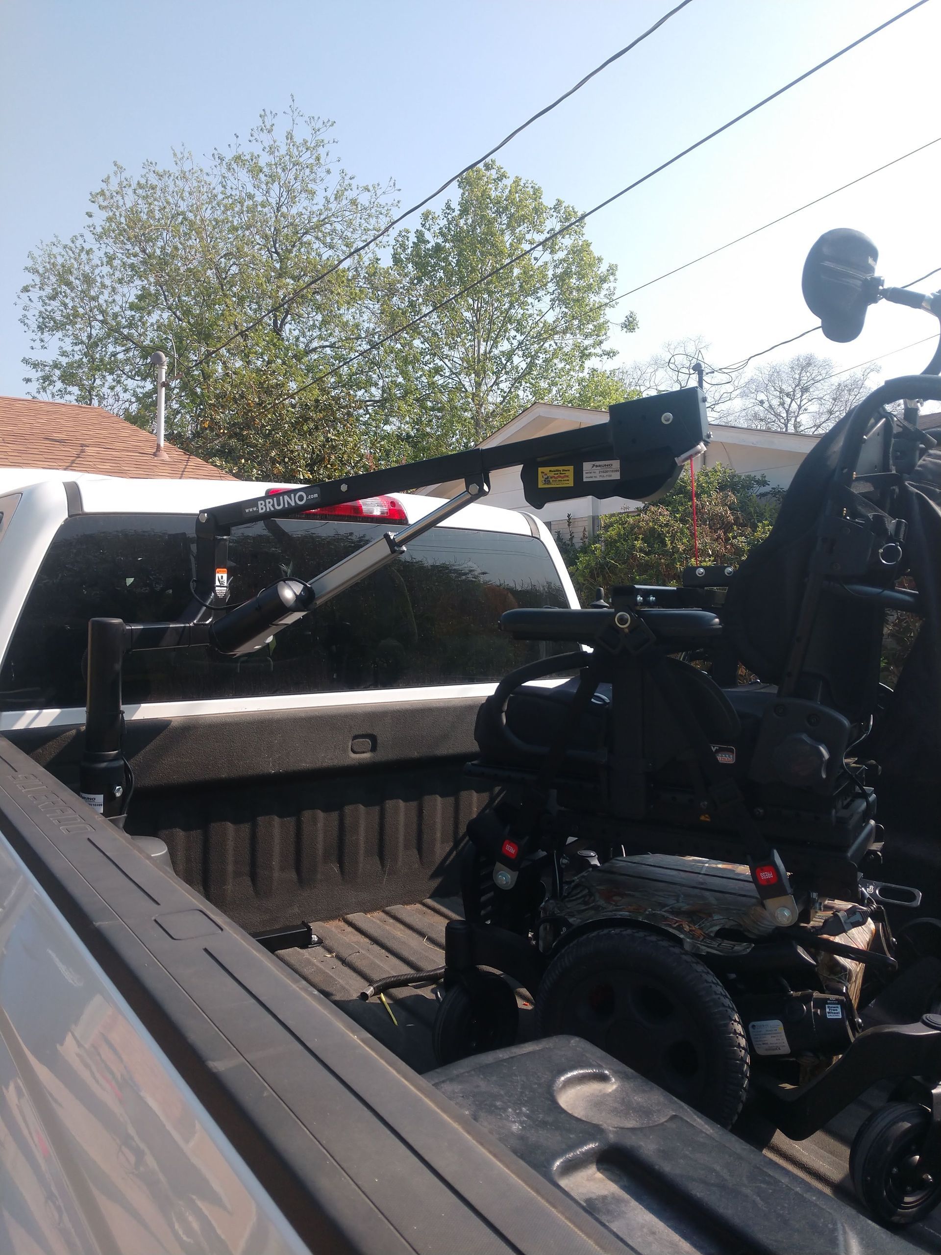 A black electric wheelchair secured in a truck bed with a lift arm.