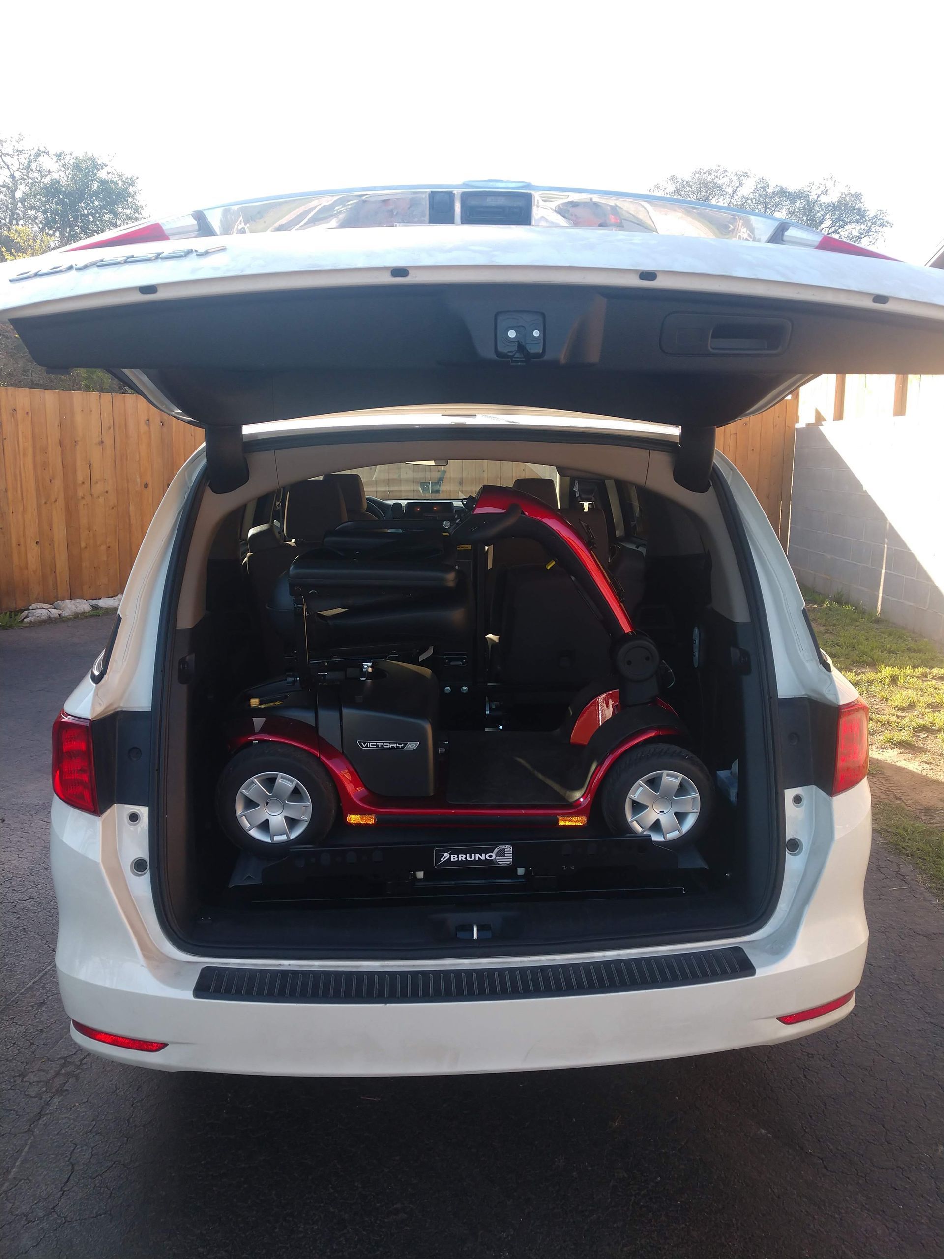 A red and black mobility scooter loaded in the open trunk of a white minivan.