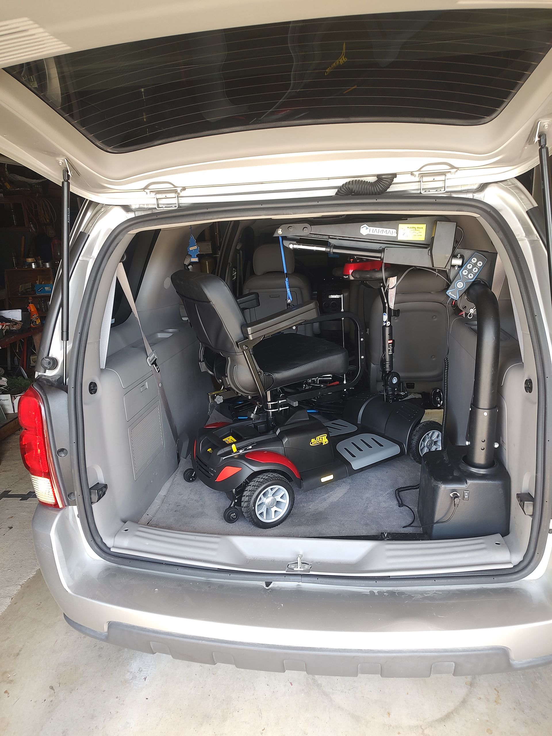 A silver minivan with its trunk open, revealing a wheelchair and mobility equipment inside.