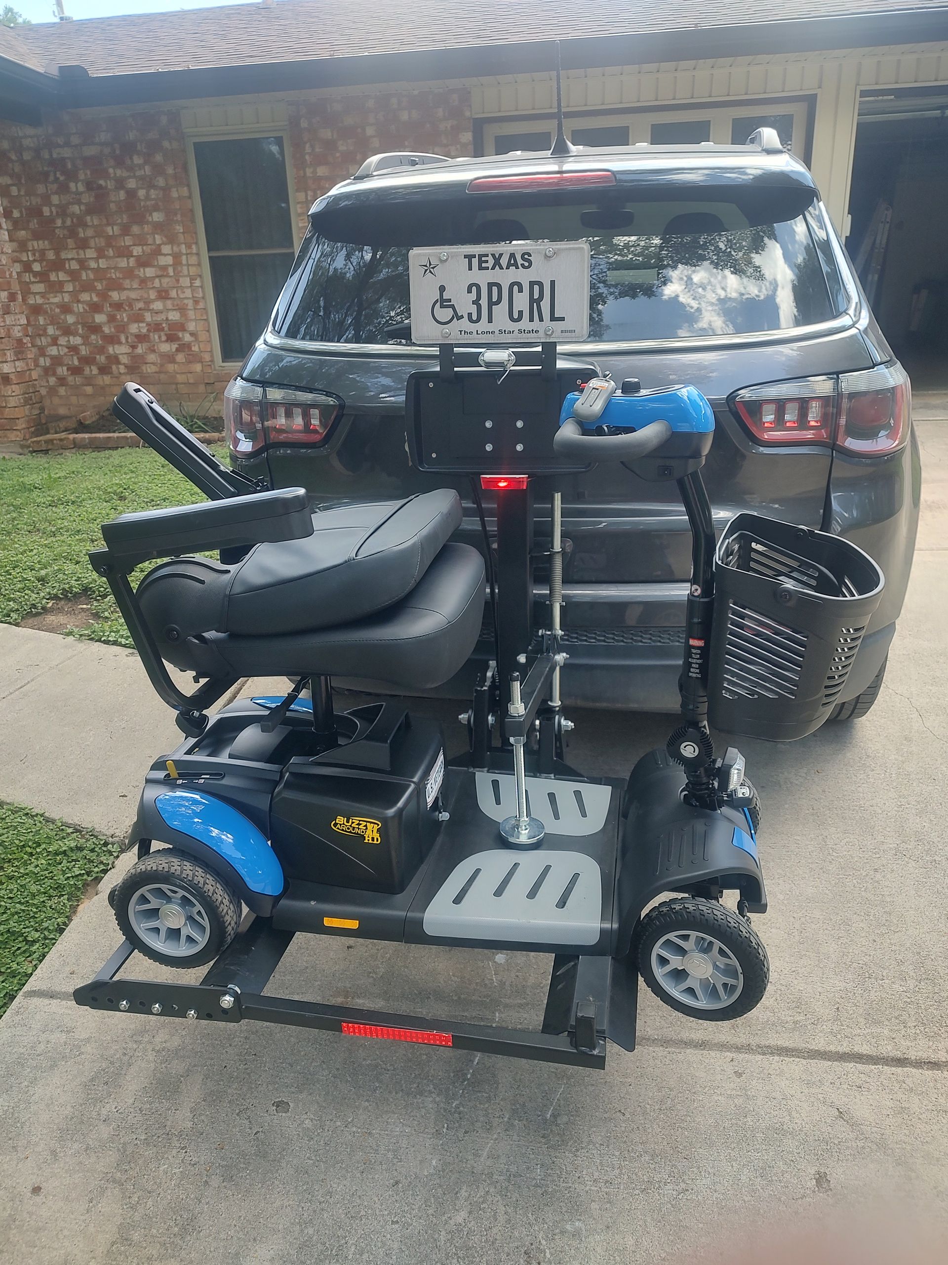 A black SUV with a Texas license plate towing a blue and black mobility scooter on a lift.