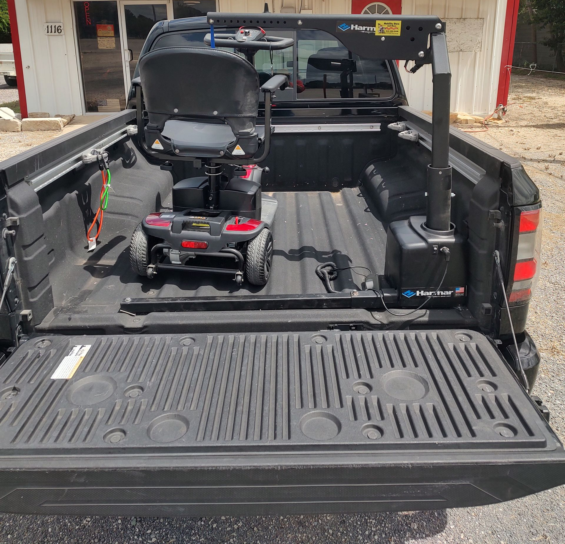Black pickup truck bed with a mobility scooter and lift. Scooter is red/black. The lift is black.