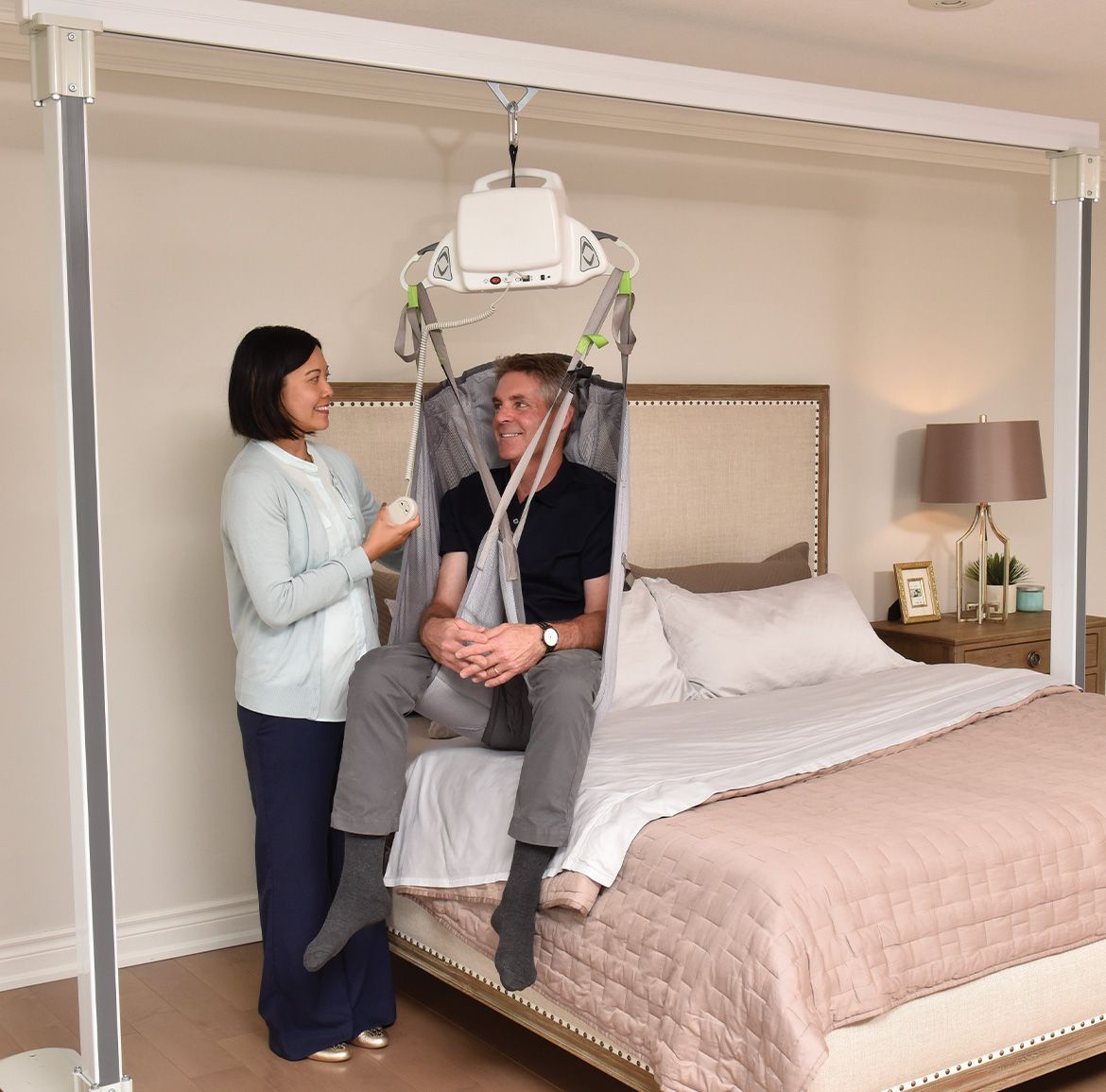 Three women demonstrate use of a patient lift on a bed with a dummy. They are reading instructions in a bright room.