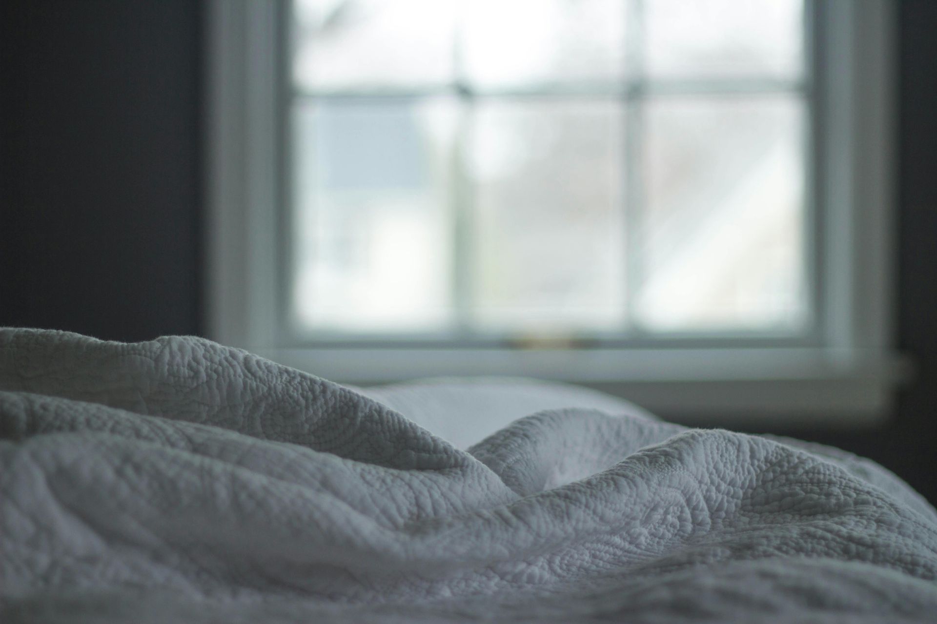 White blanket on bed, blurred window in background.