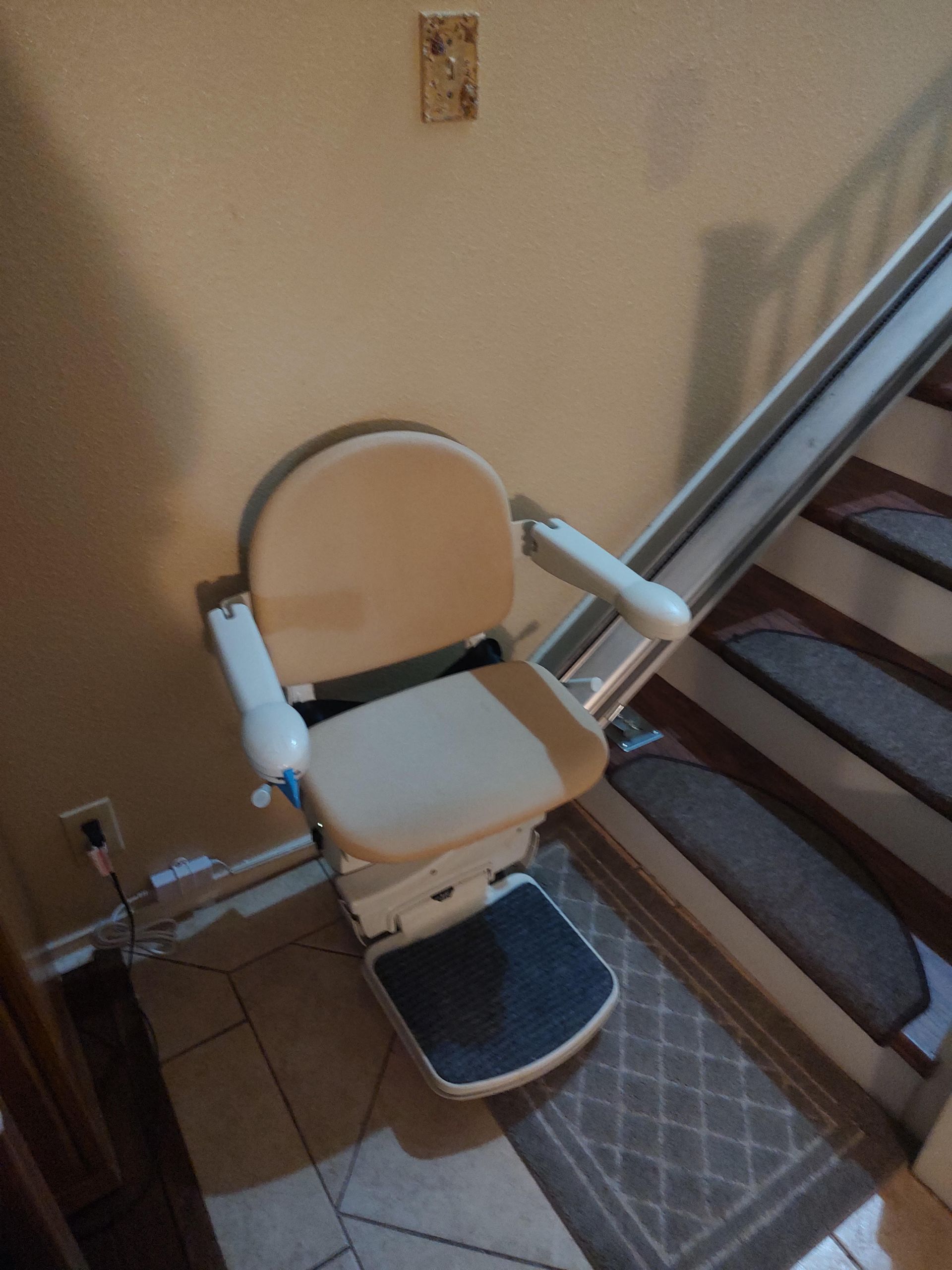 A stairlift chair on a staircase, tan and white, with a person's stairs in the background.
