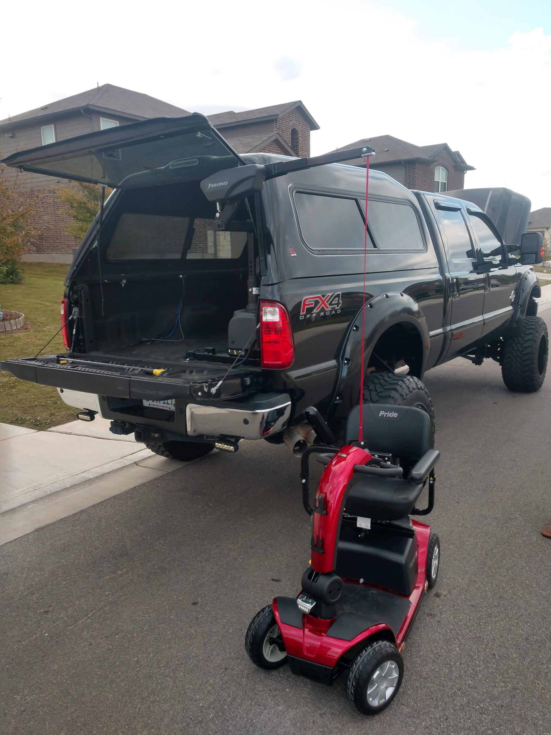 A black pickup truck bed with a wheelchair lift secured by a red strap.