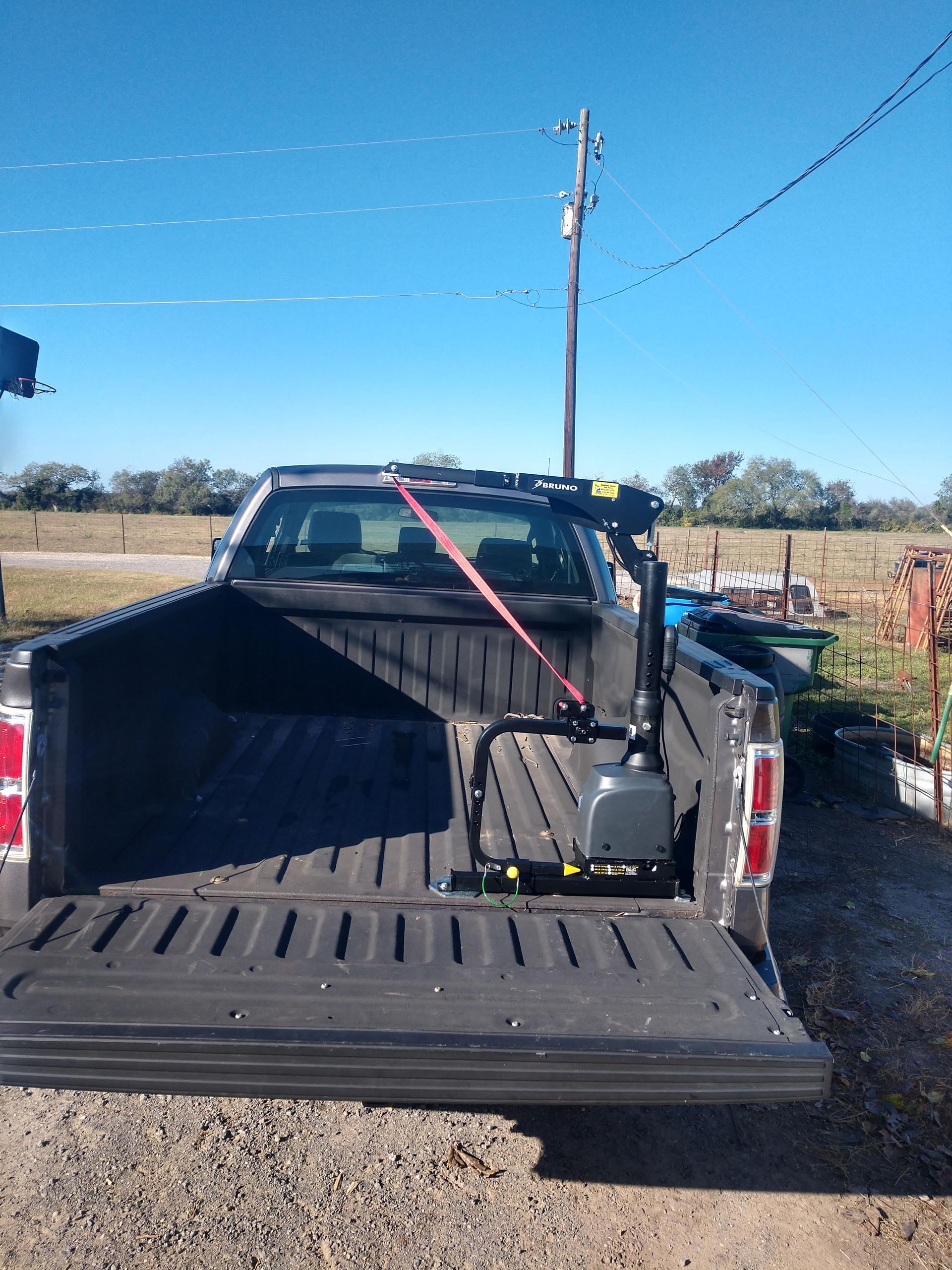 A black pickup truck bed with a wheelchair lift secured by a red strap.