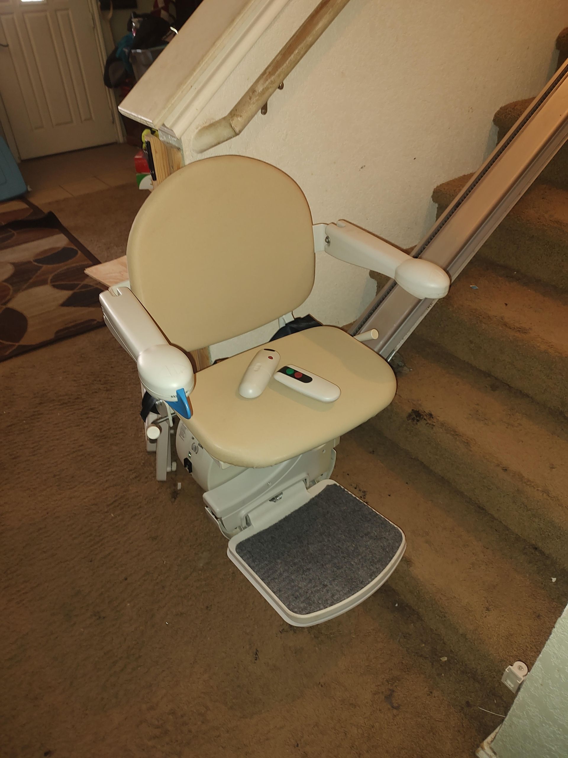 Beige stair lift chair on a staircase. A remote sits on the armrest.