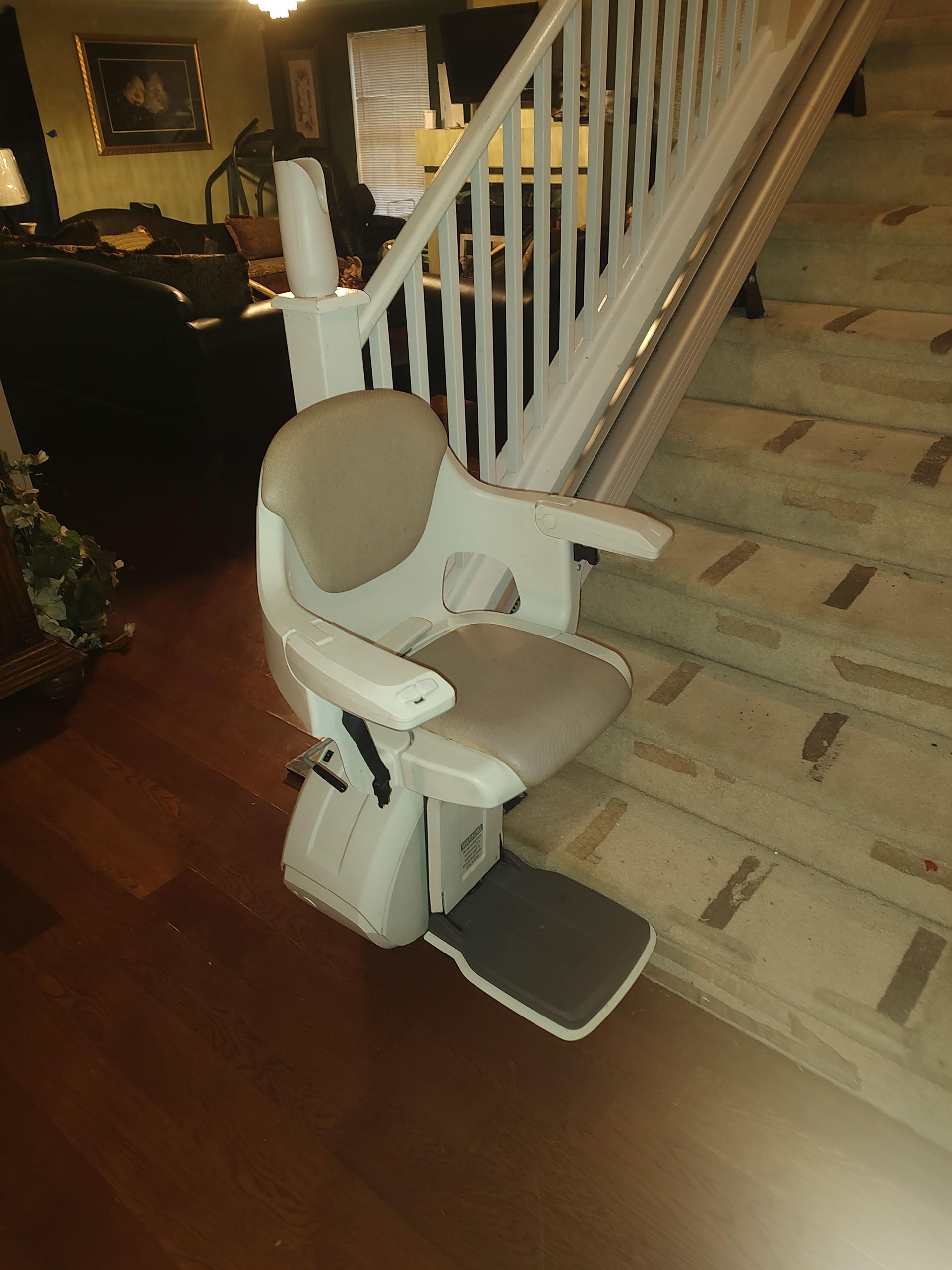 A stair lift with a tan seat and footrest on a brick and wooden staircase.