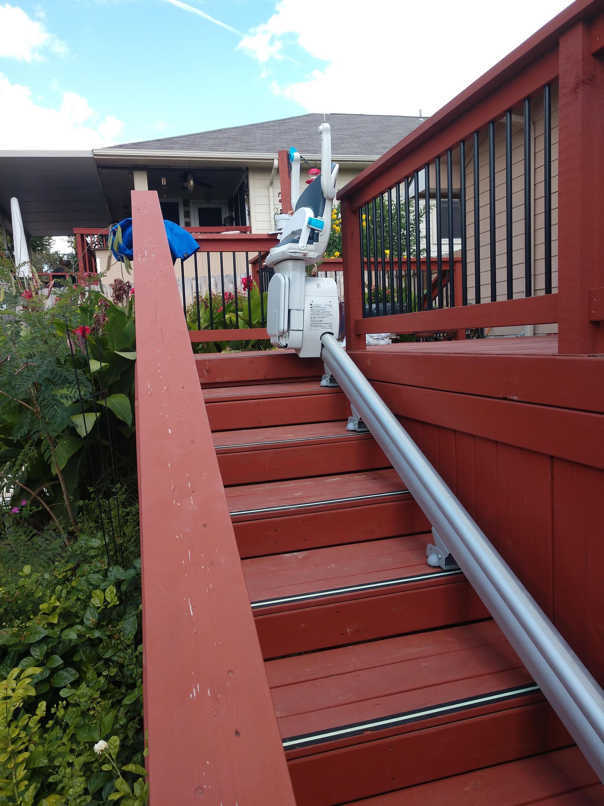 Red wooden deck stairs with a chair lift, leading to a house with a deck.