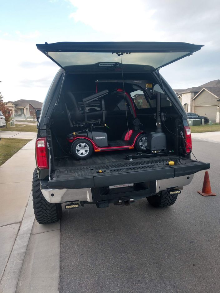 Red mobility scooter inside a truck bed with the tailgate down, parked on a street.