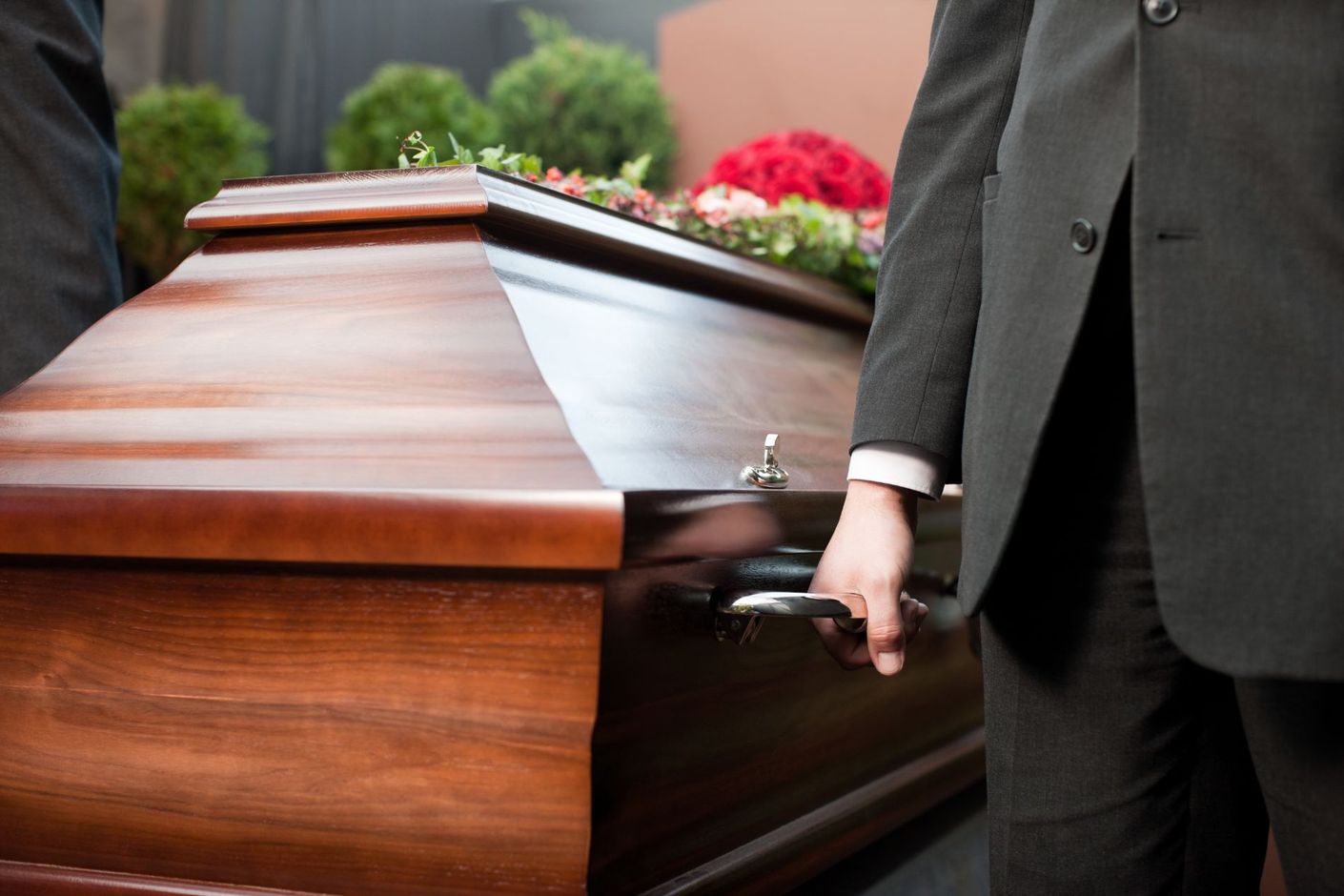 Uomo in abito scuro in piedi accanto a una bara di legno lucido all'aperto