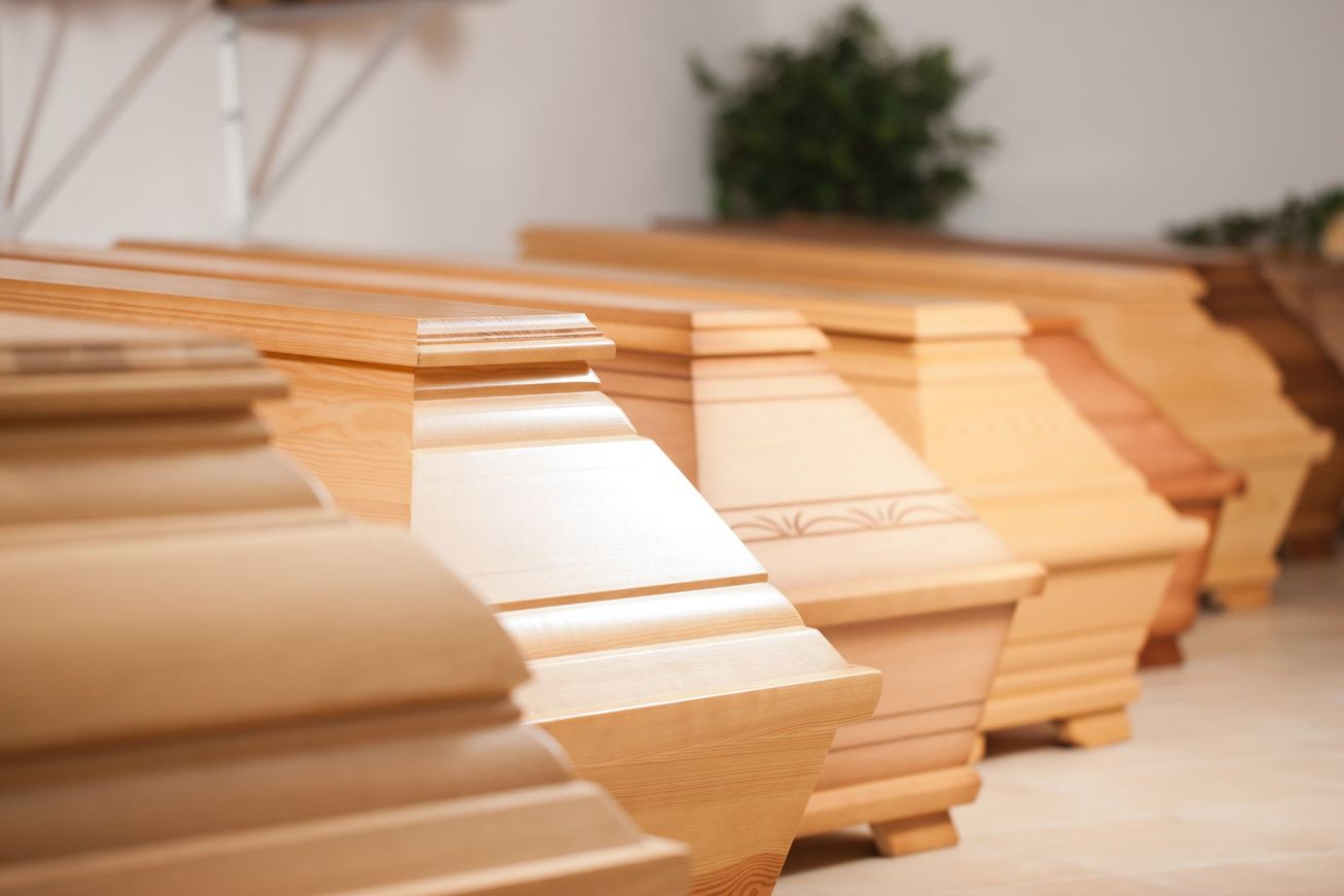 Bare di legno con coperchi lucidati, disposte in una sala espositiva di pompe funebri.