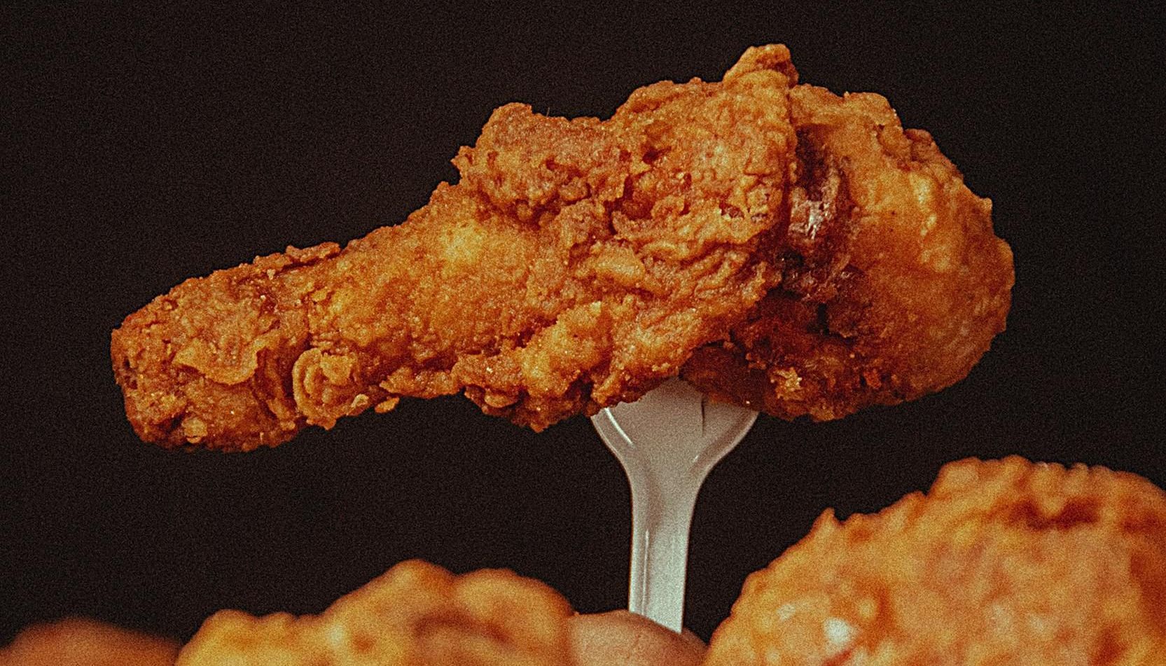 A person is holding a piece of fried chicken on a plastic fork.