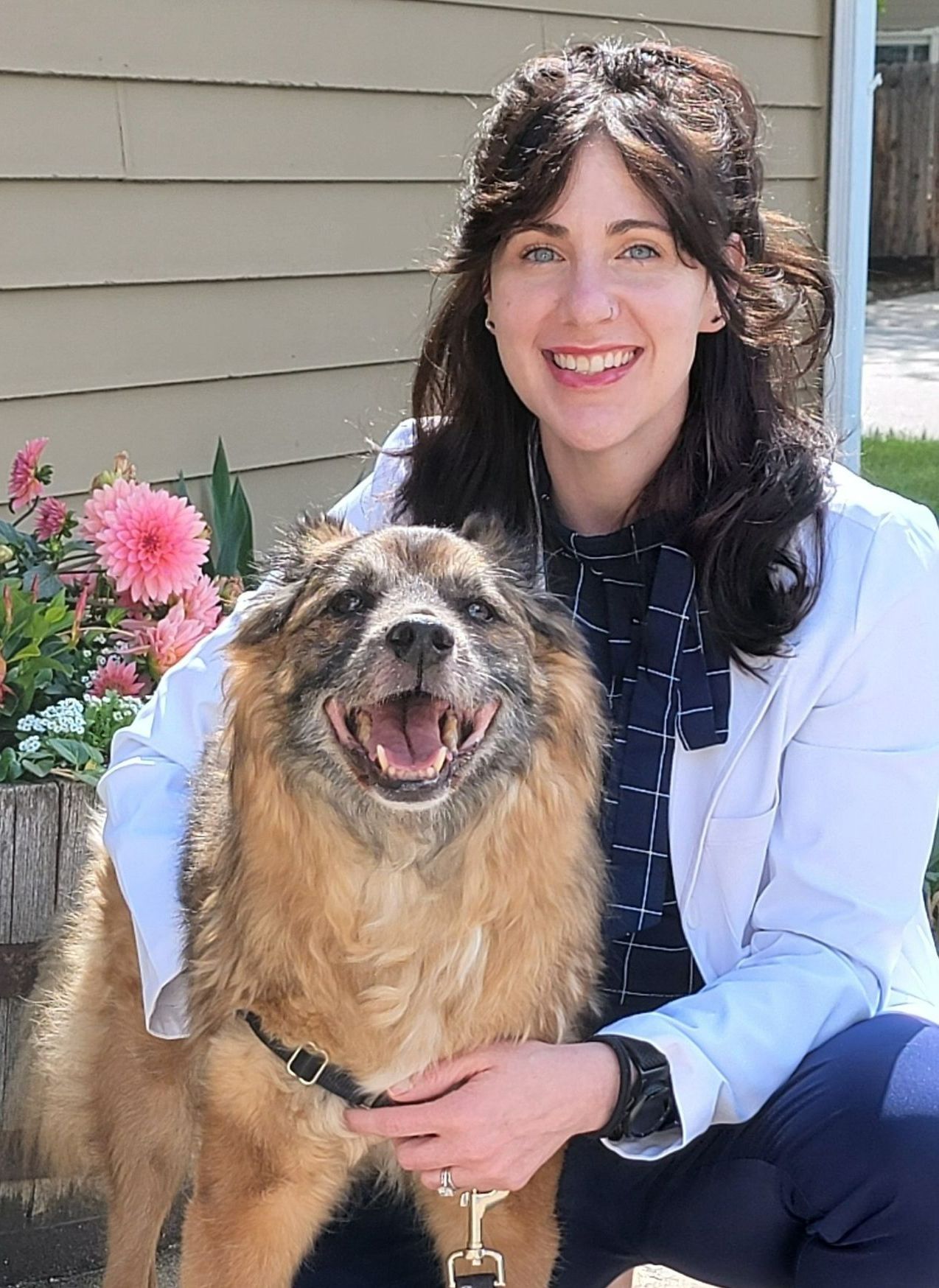 A woman in a white coat is kneeling down next to a brown dog.