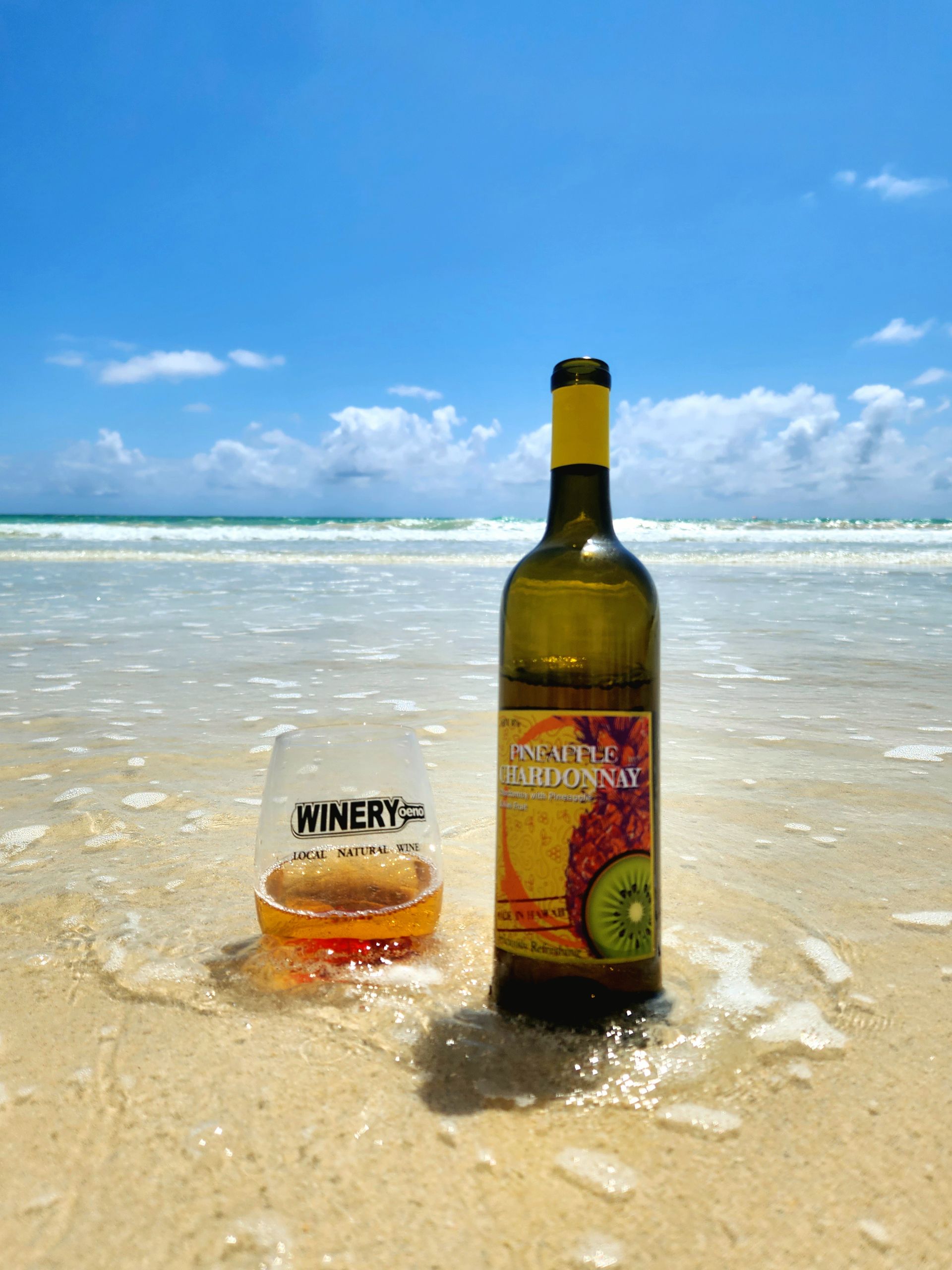 Glass And Bottle Of Wine Are On The Beach | Kailua, HI | Oeno Winemaking