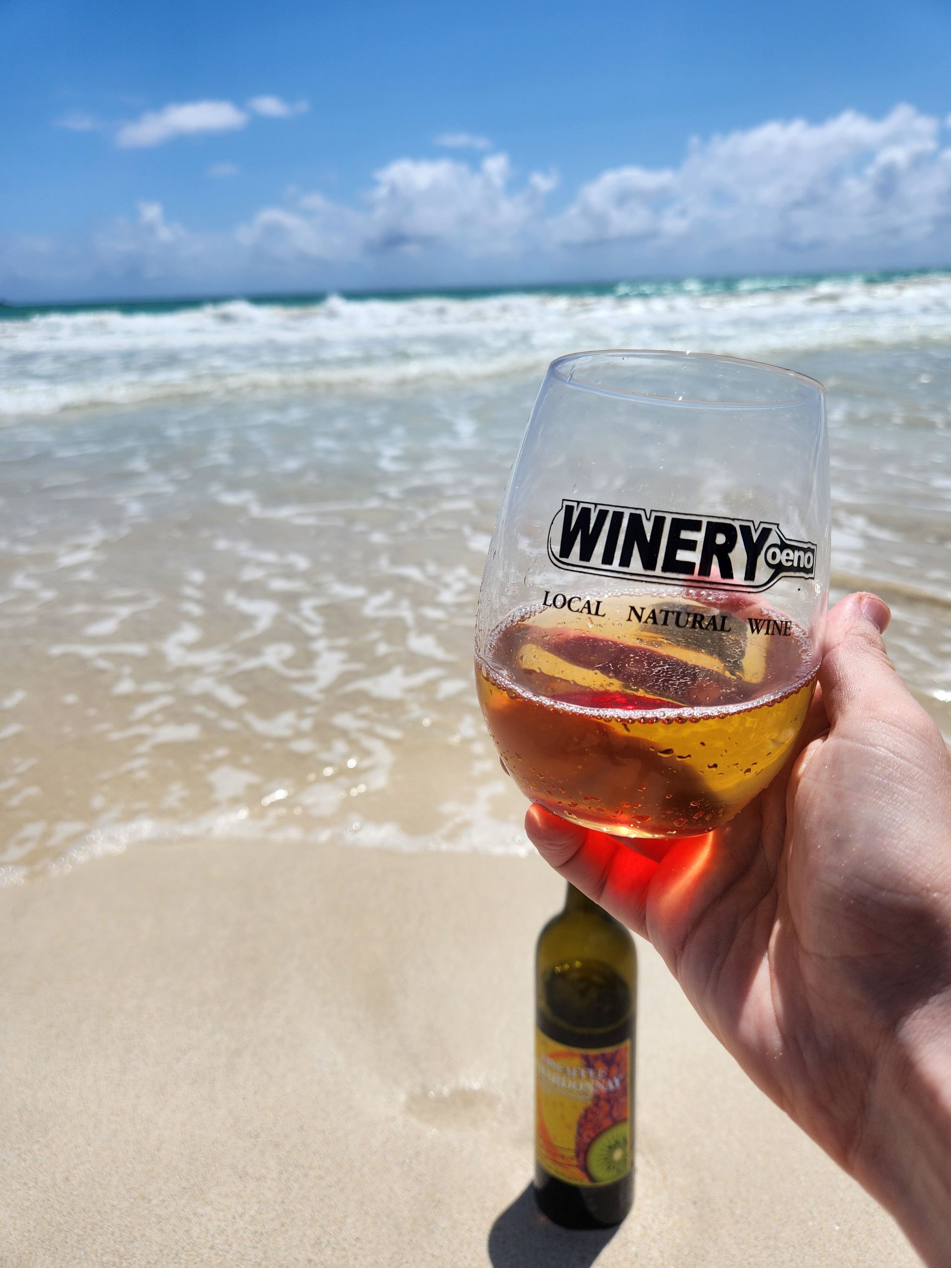 A Person Is Holding A Wine Glass On The Beach | Kailua, HI | Oeno Winemaking