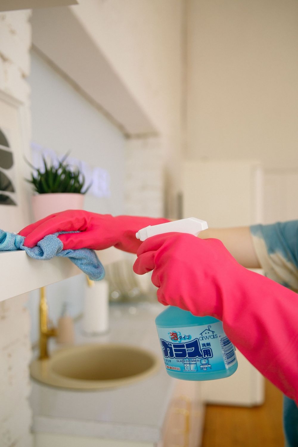 Gloved hands cleaning a sink with a spray bottle in a bathroom