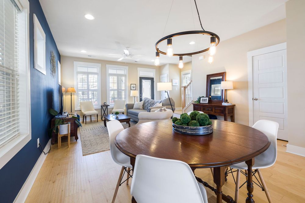 Bright dining area with round wood table, white chairs, blue accent wall, and chandelier lighting