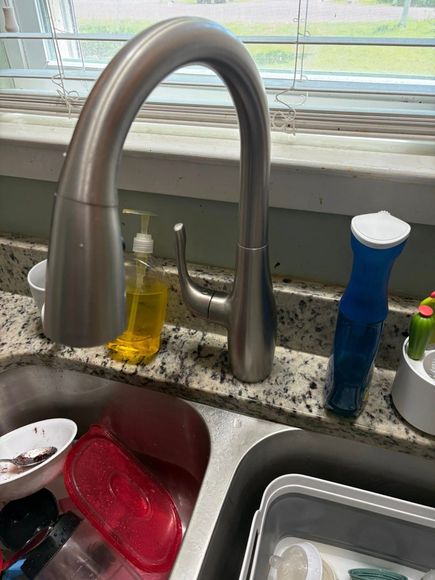 Kitchen sink with a tall, curved faucet, dirty dishes, and soap dispensers on a speckled countertop.