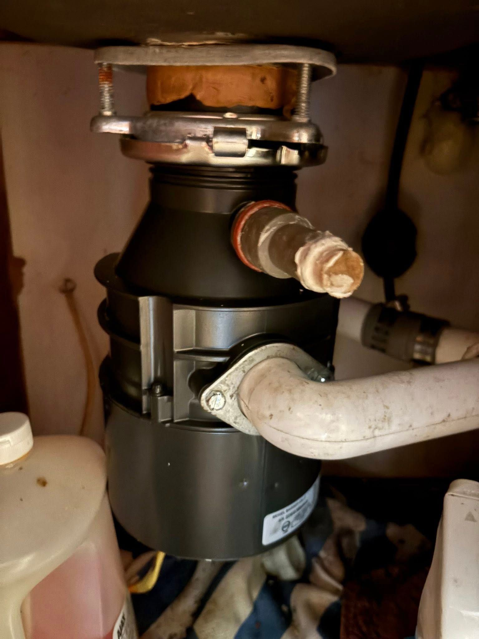 Garbage disposal under a sink; black and silver device with plumbing.
